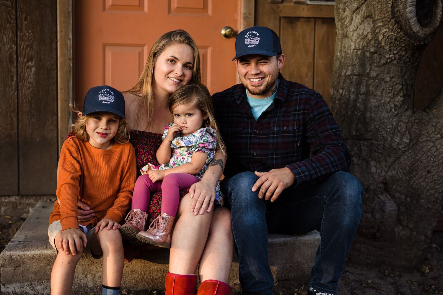 People relaxed and smiling while sitting on wooden steps in front of an orange door.
