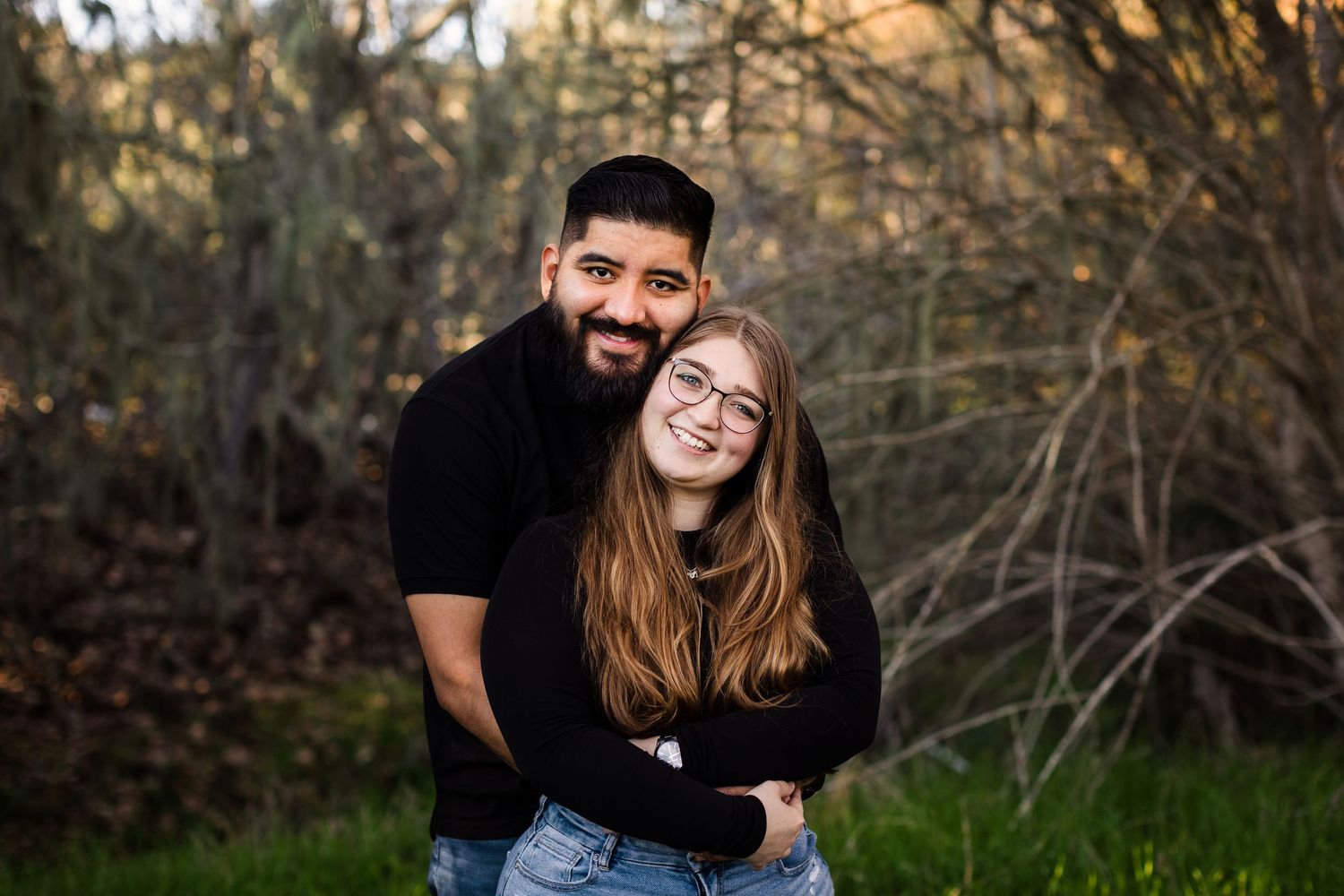A loving couple sitting outdoors in a park sharing tender moments during a photo session in natural lighting.