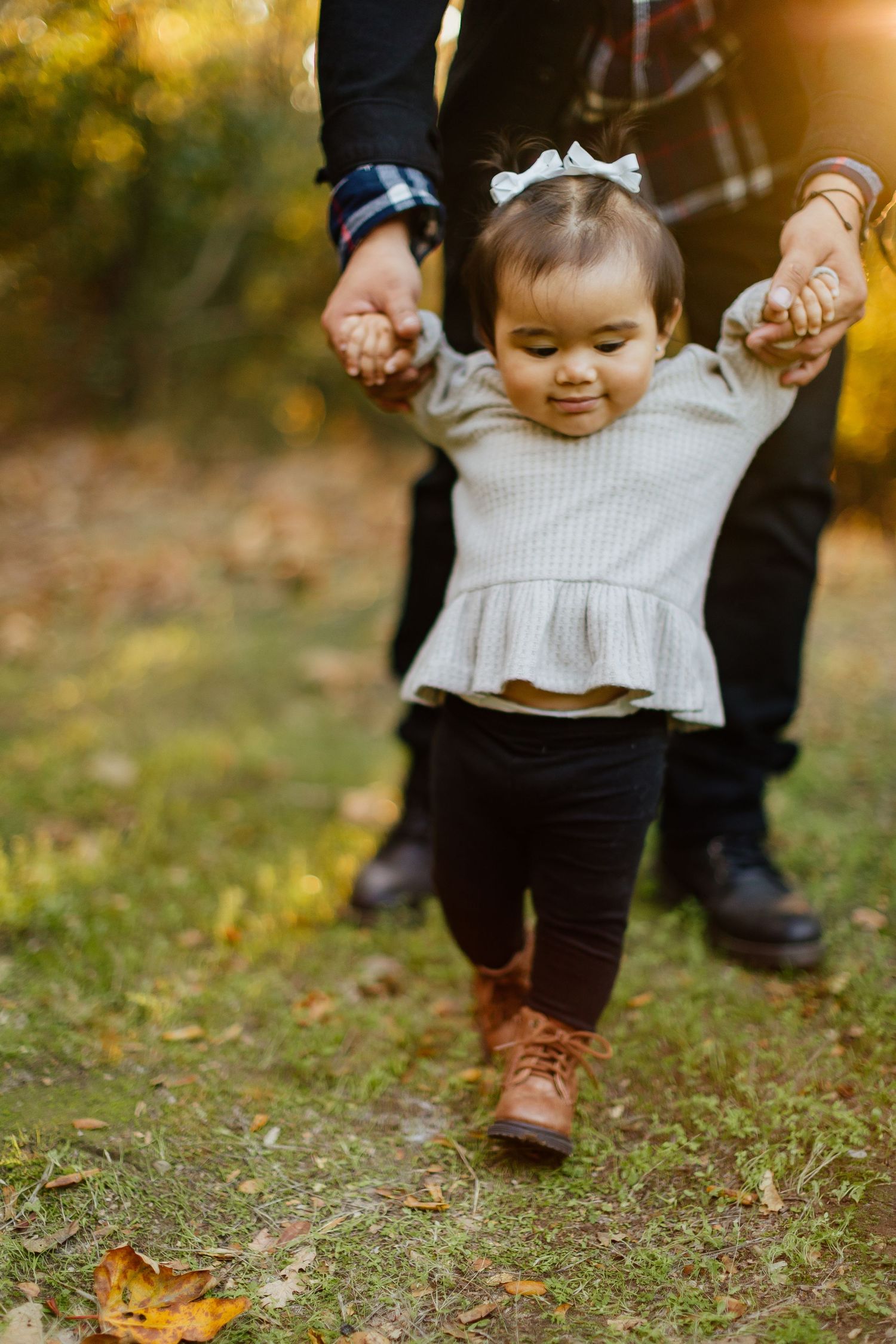 Close-up view of people's legs and feet walking together on grass during fall with autumn leaves scattered on ground.
