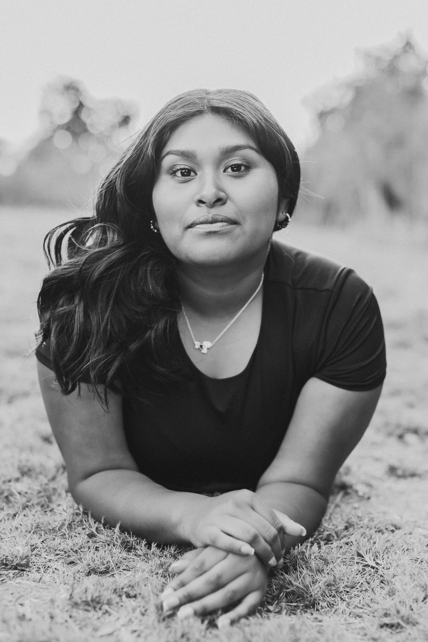 Black and white portrait of young woman with long hair lying on grass looking at camera.
