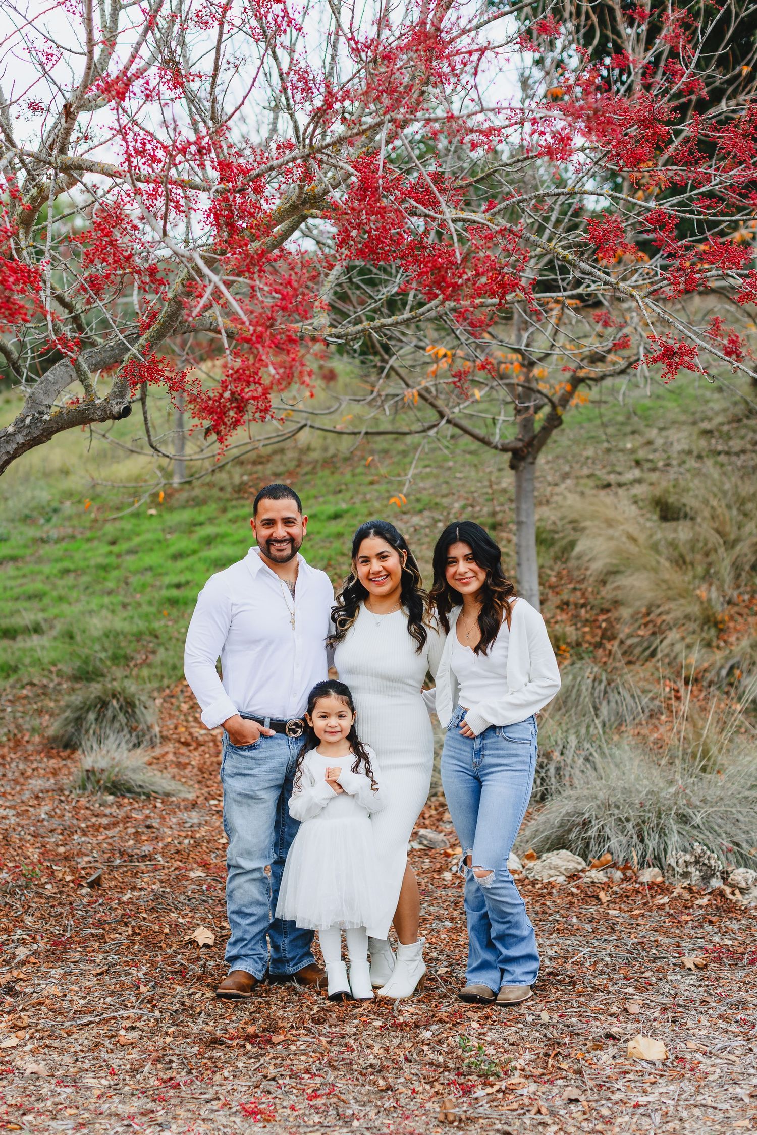 A family of four poses together under a blooming red tree during fall.