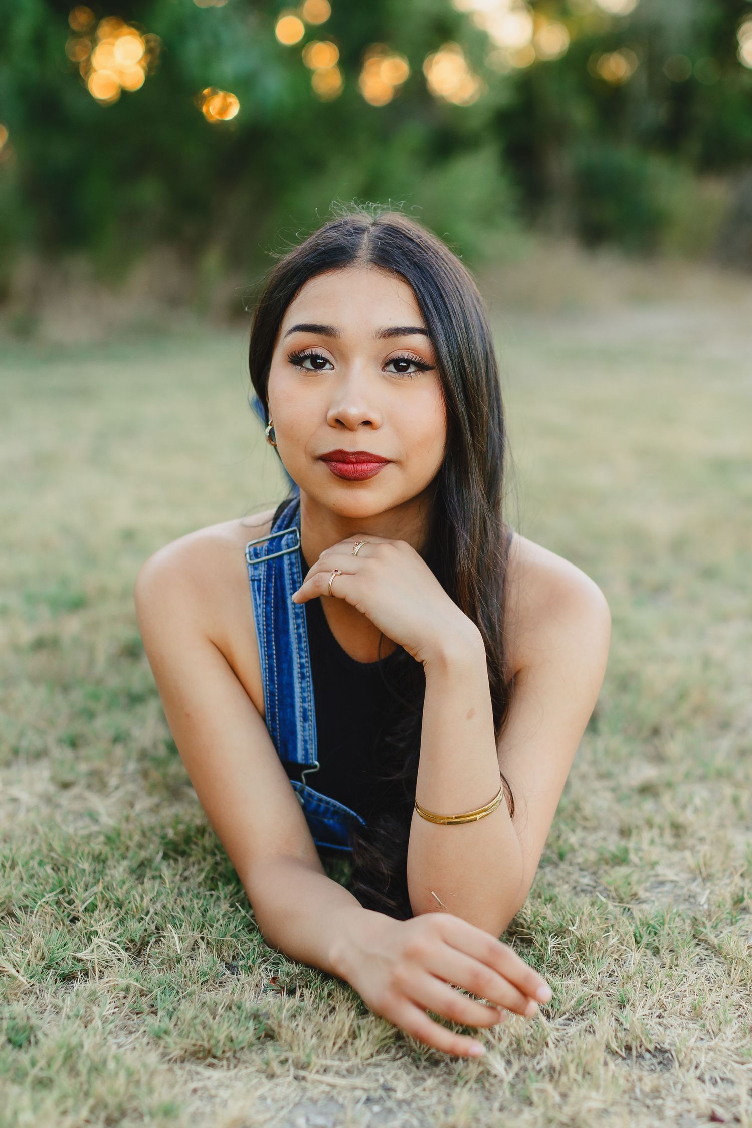Person in denim overalls lying on grass during golden hour portrait session.