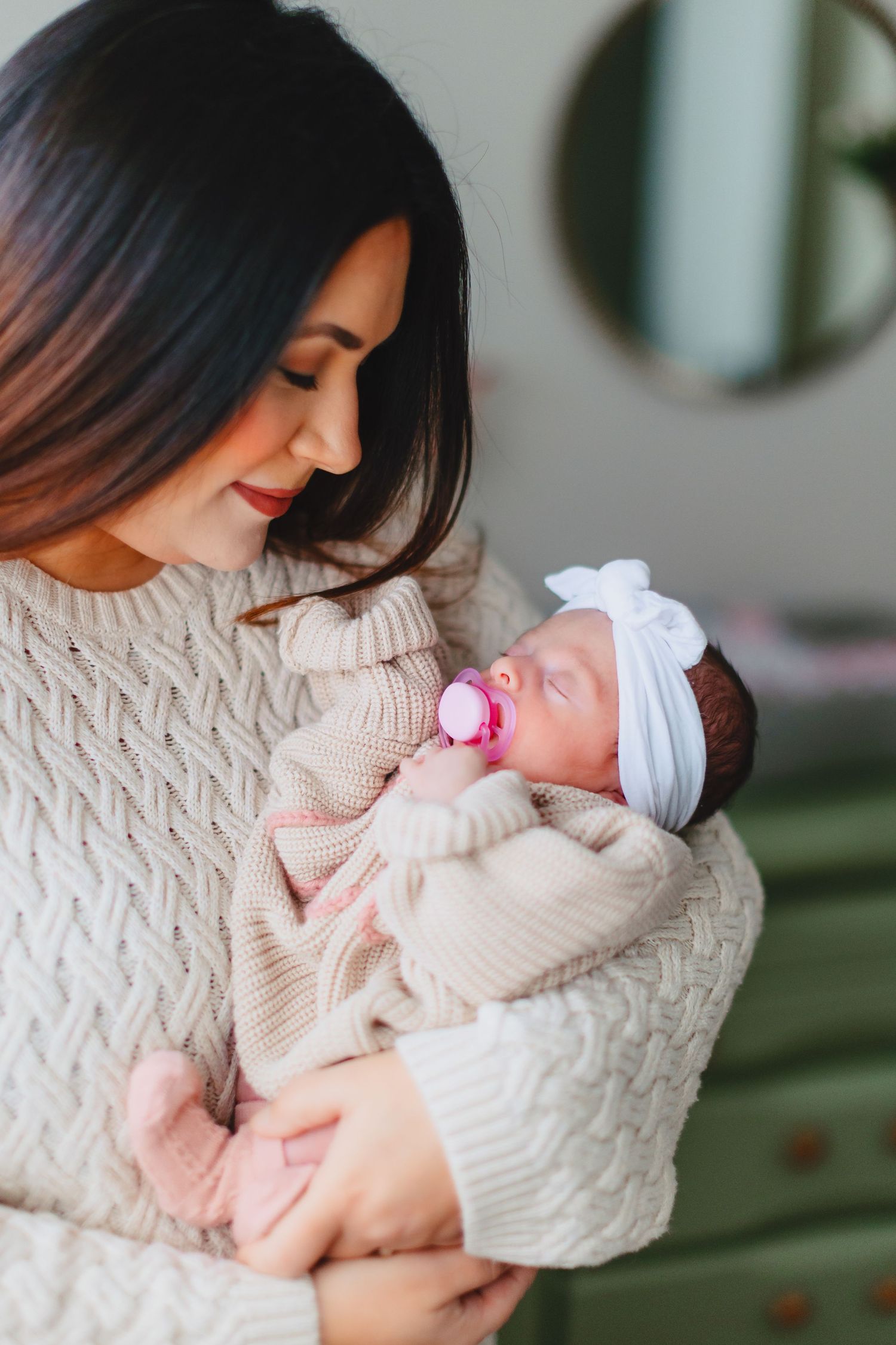 Mother in cream sweater holding sleeping newborn wrapped in cozy blanket.