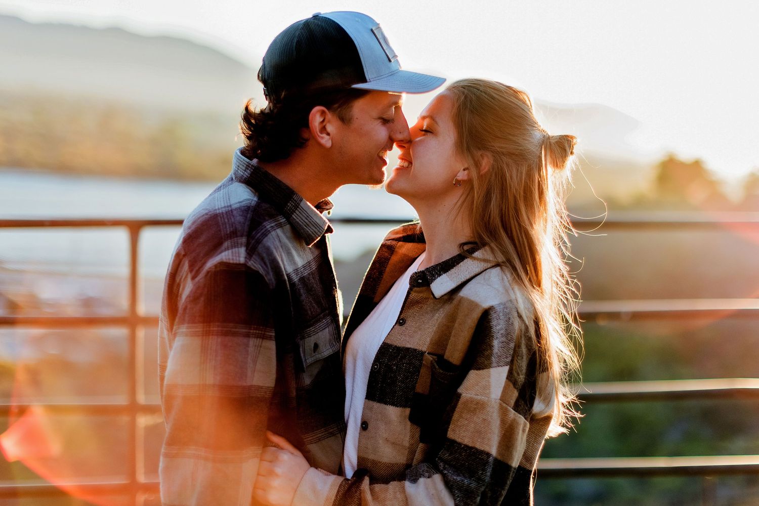 Couple sharing romantic moments at sunset by a railing with golden light illuminating their silhouettes.
