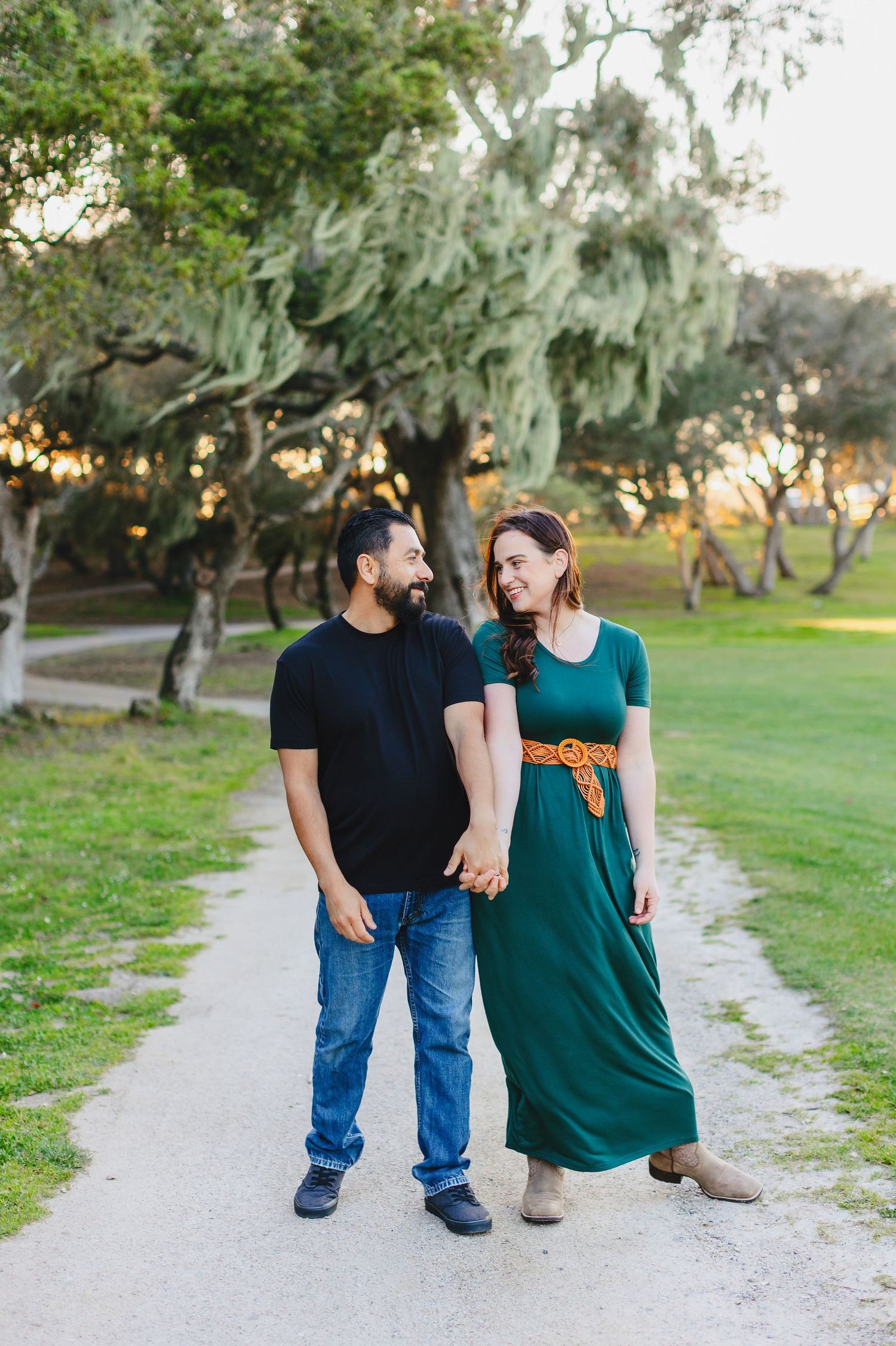 Couple in casual attire walking together on path surrounded by trees.