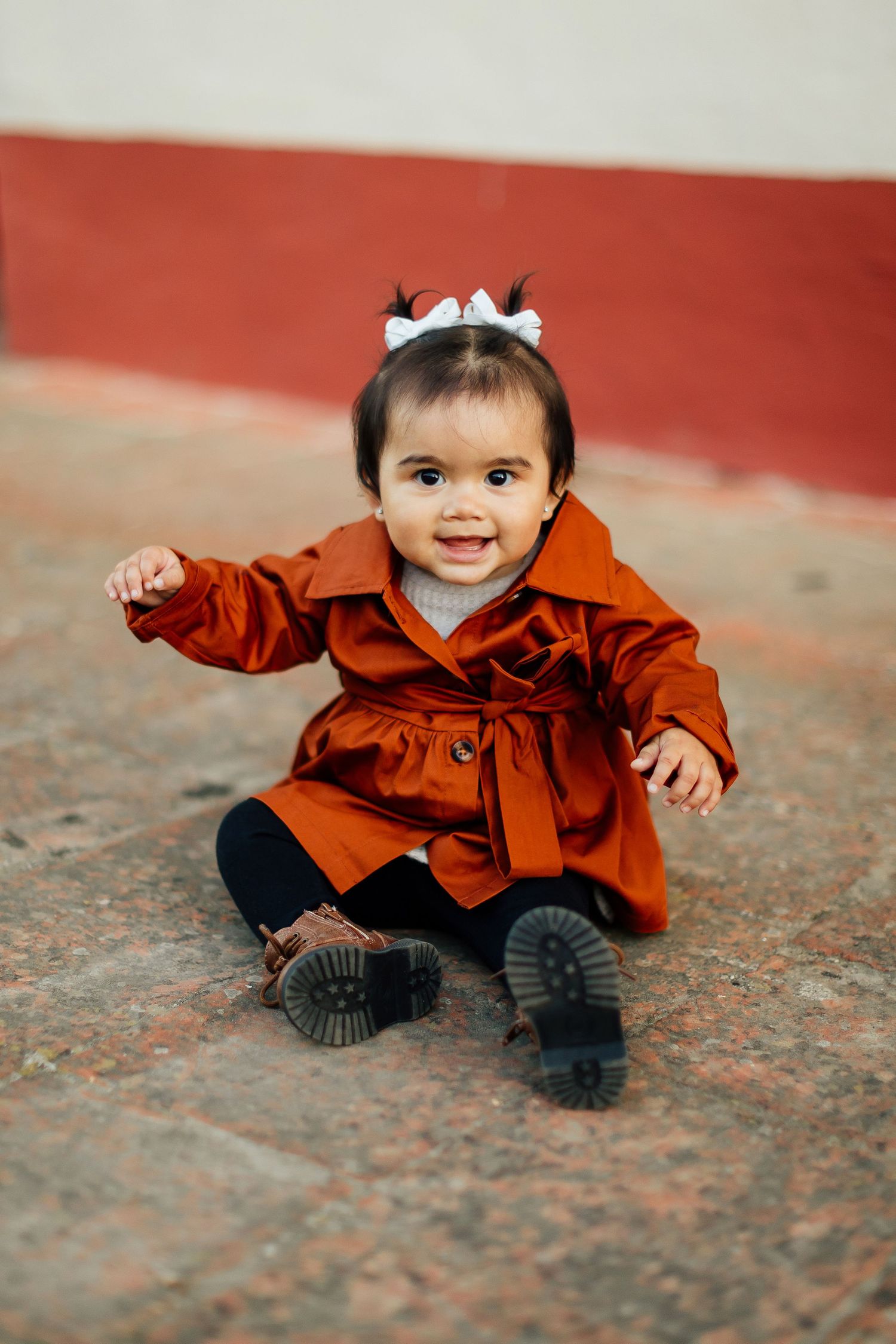 A small child wearing a brown jacket and black pants sits playfully on the ground in multiple similar poses.