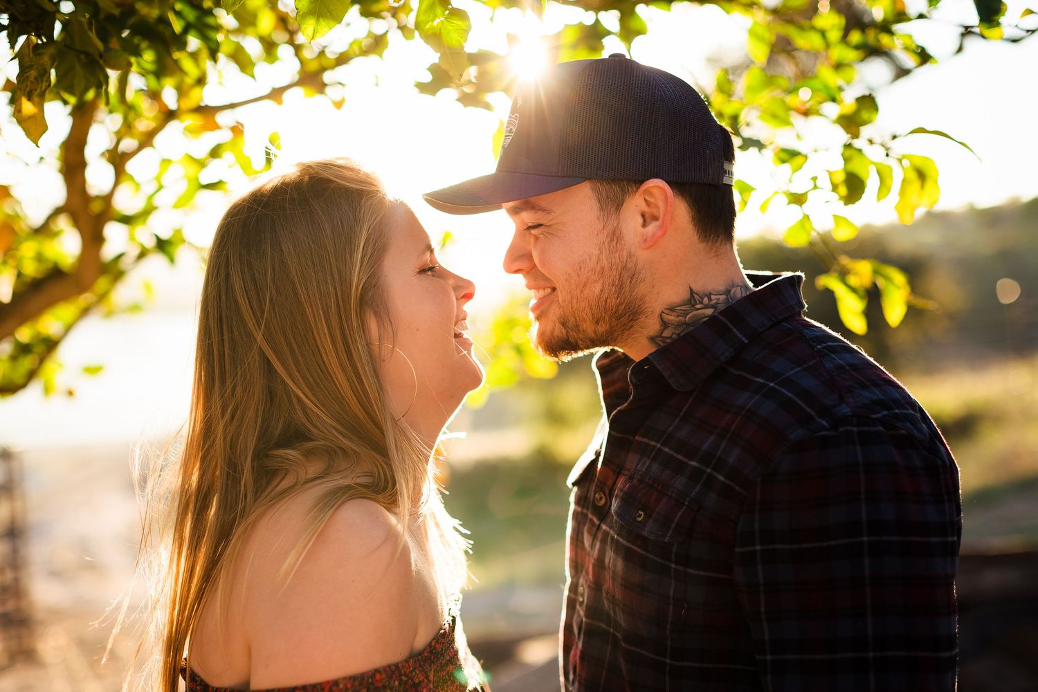 A couple shares a tender moment in golden sunlight beneath tree branches during a romantic outdoor photoshoot.