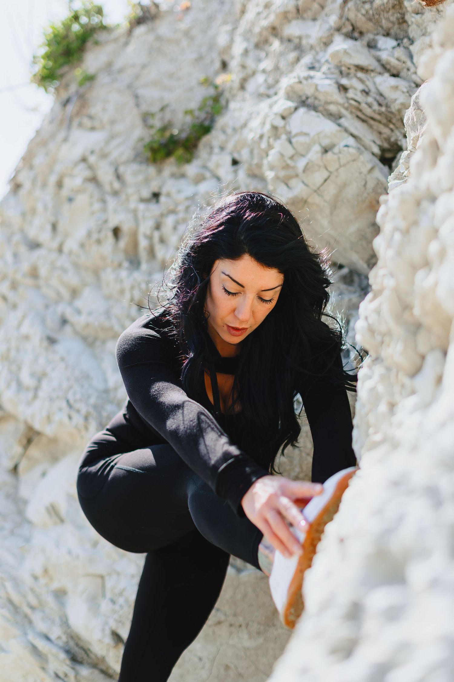 Athletic woman in black outfit stretching on white rocky terrain during outdoor workout.