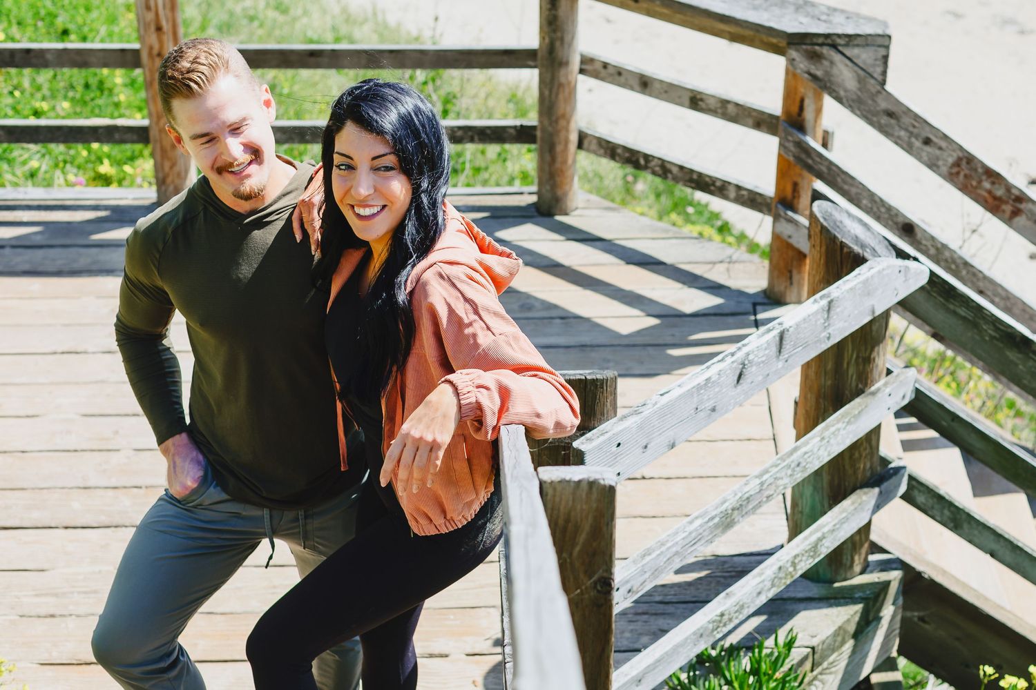 Two people in casual attire sharing a happy moment together on a wooden boardwalk on a sunny day.