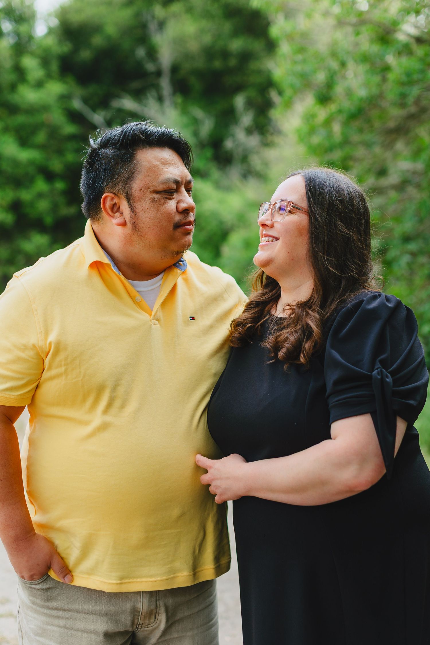 A couple shares a joyful laugh together while standing outdoors in a natural green setting.