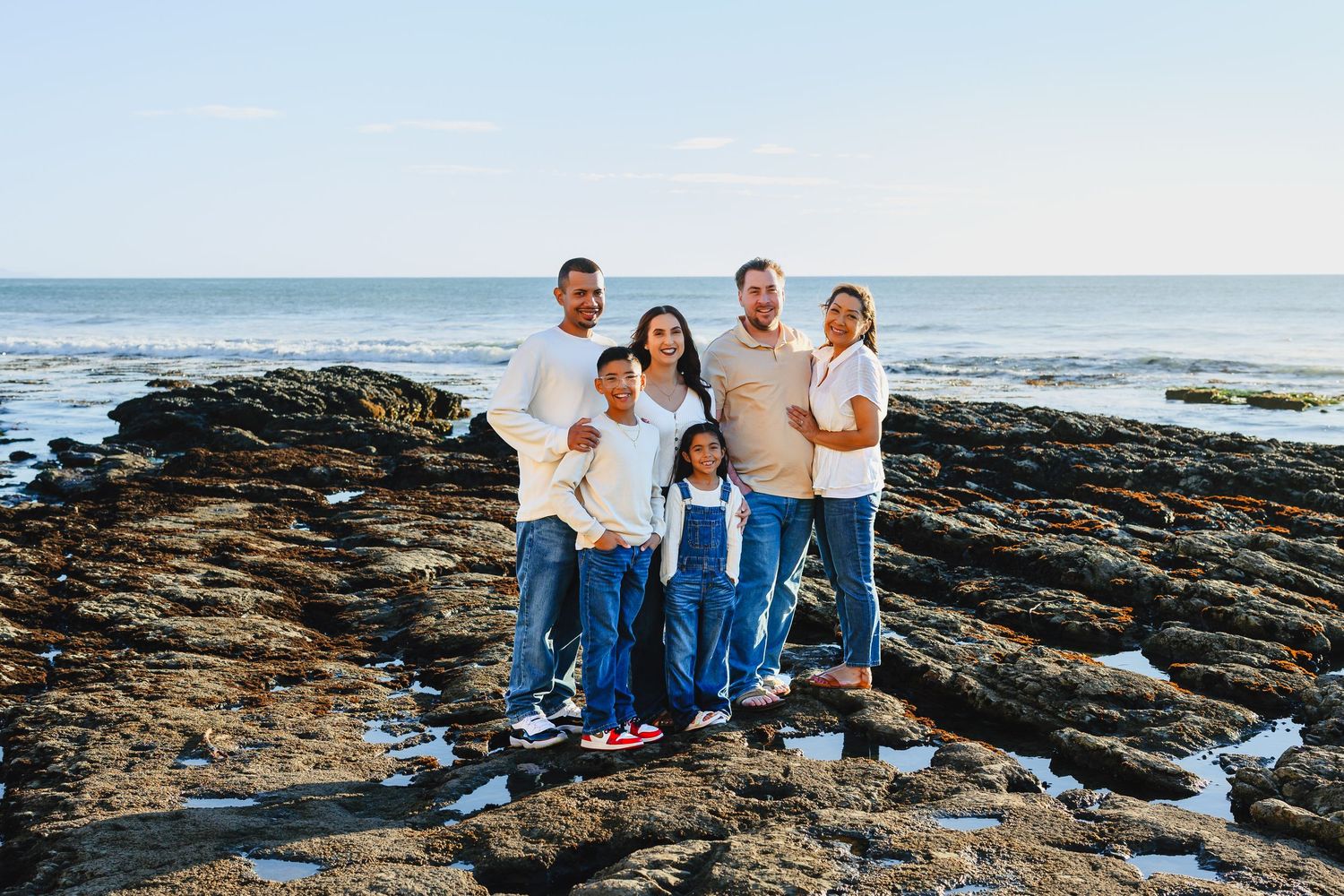 A family sits together on rocky coastal outcrops during a beach photoshoot at sunset.