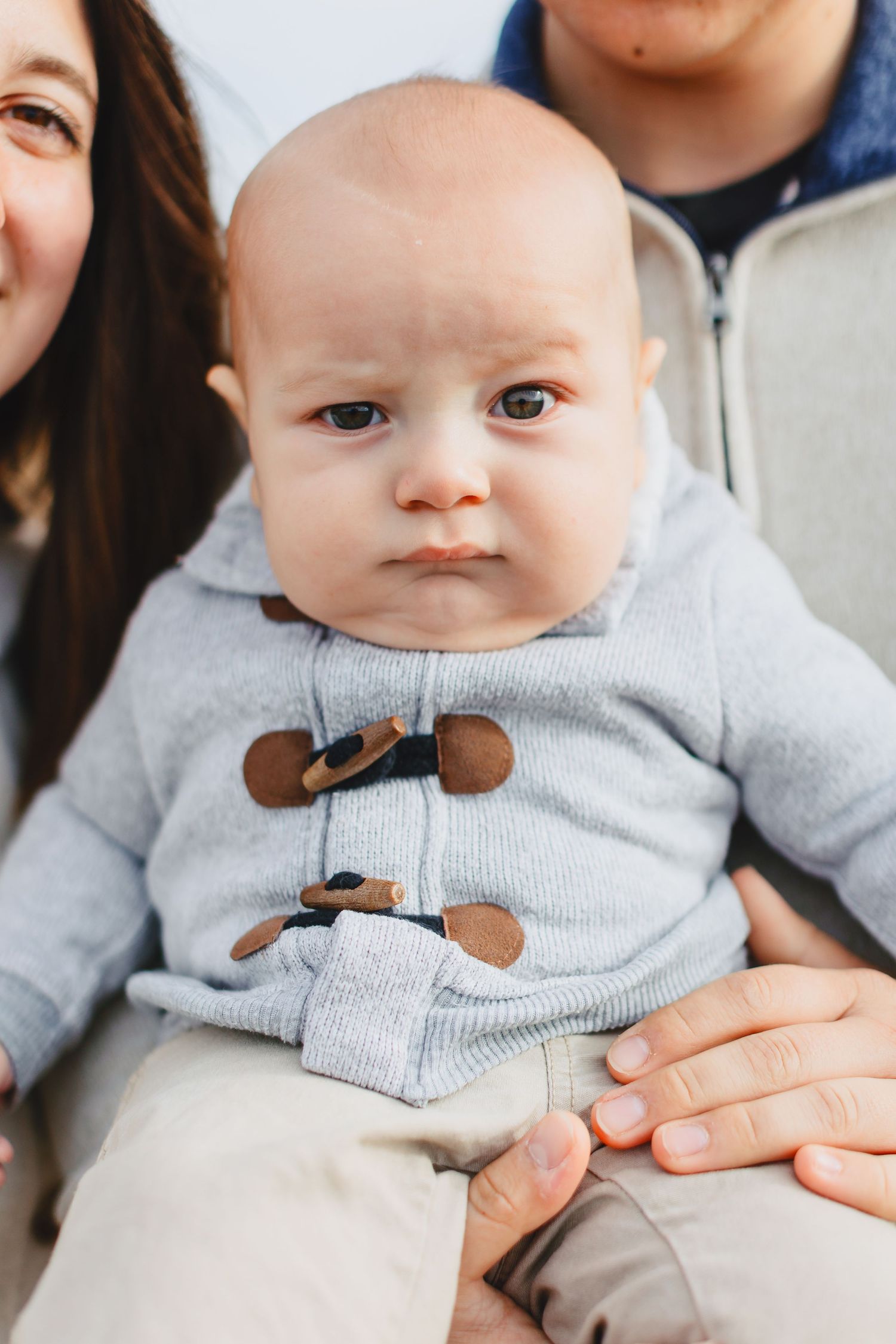 Baby wearing a grey toggle coat sitting on someone's lap.