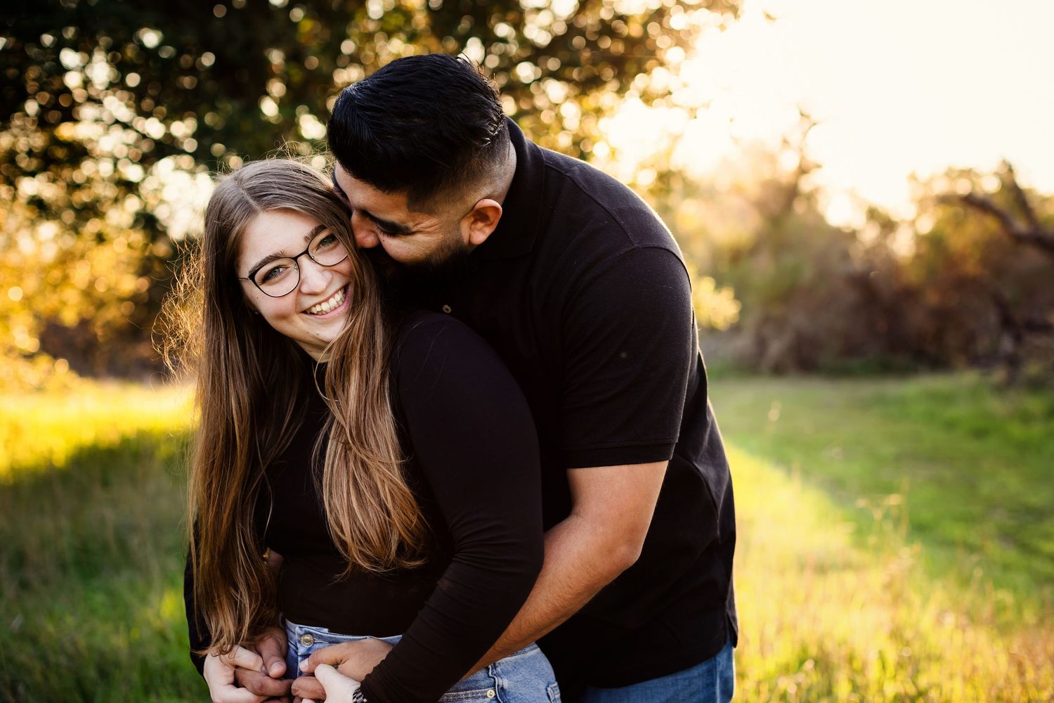 A couple shares a tender moment in a sunlit meadow during a romantic outdoor photoshoot at golden hour.