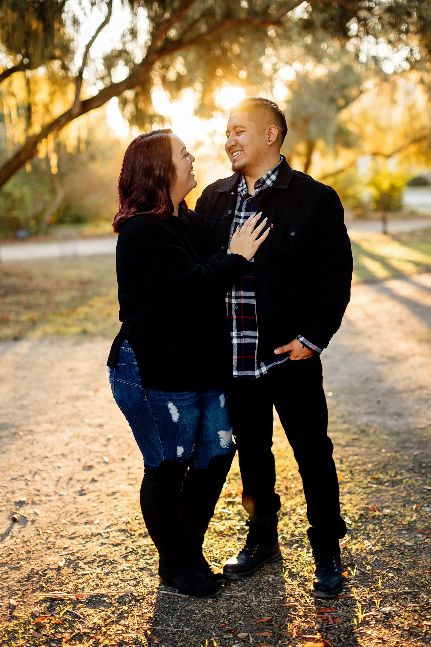 Couple in casual attire shares tender moments at sunset in an autumn park setting while surrounded by fallen leaves.