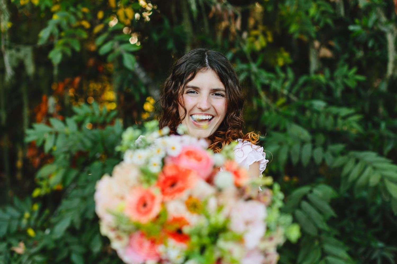 Vibrant bouquet of coral and peach flowers with greenery against a lush garden background.