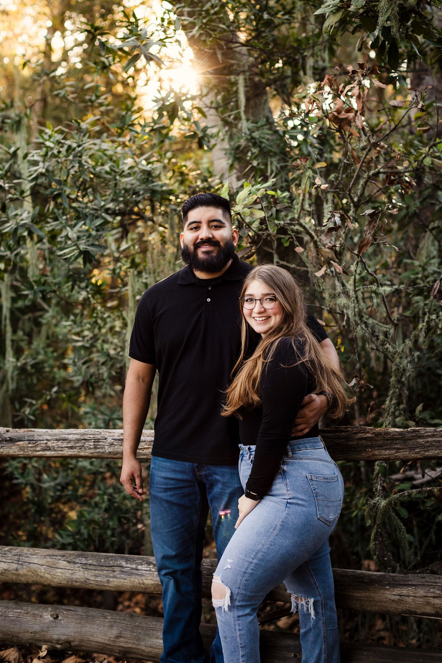 Couple sharing joyful moments together while sitting on a wooden log surrounded by lush greenery in a natural setting.