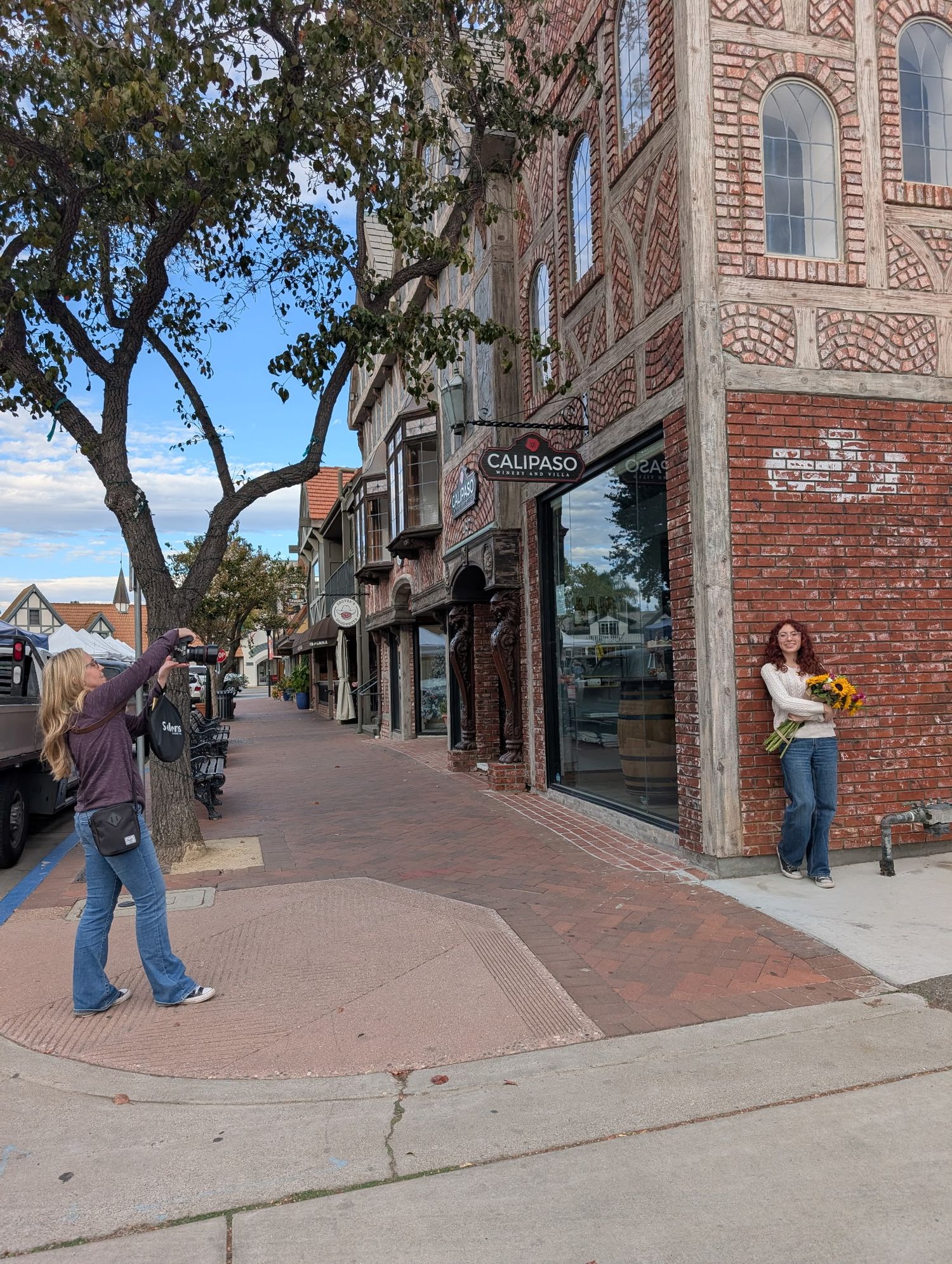 Photographer capturing a woman holding sunflowers outside Calipaso on a brick sidewalk in a charming downtown shopping district.