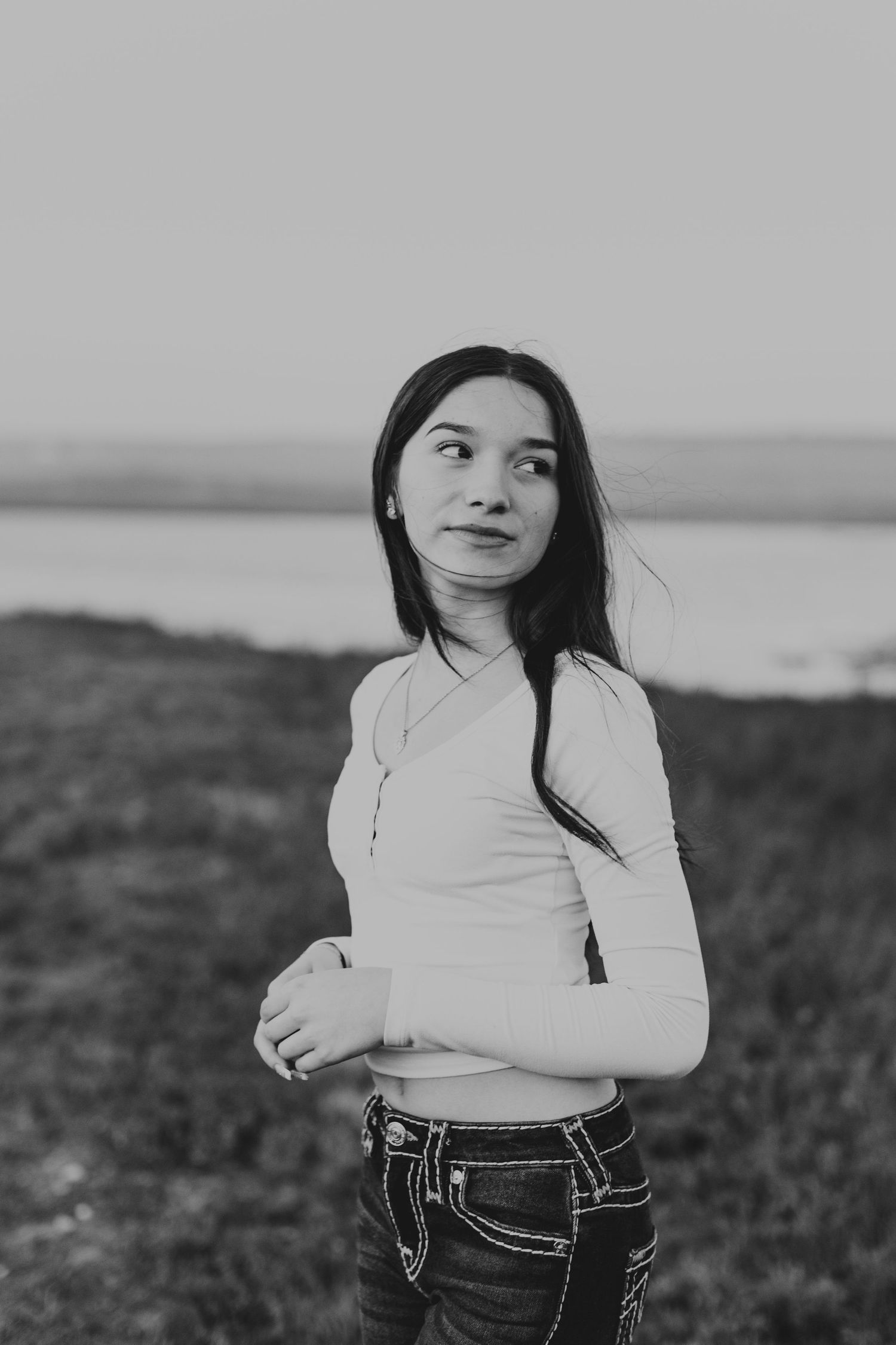 Person in white long sleeve top looking to side against coastal landscape in black and white.
