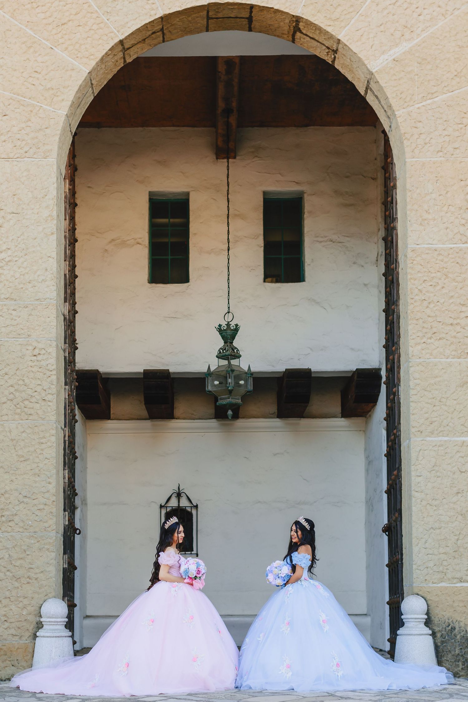 Two ballgowns, one pink and one blue, frame an archway entrance of a historic building.