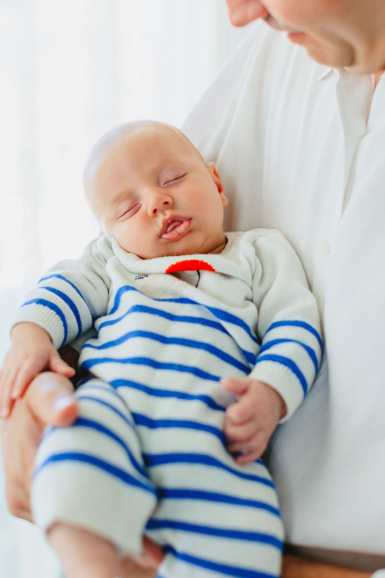 Newborn baby sleeping peacefully in mother's arms, wearing a blue and white striped onesie.
