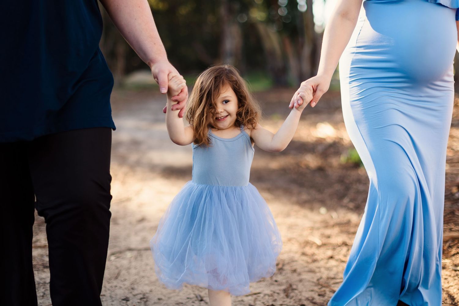 A couple dances together outdoors in formalwear, with the woman wearing a light blue dress in natural lighting.