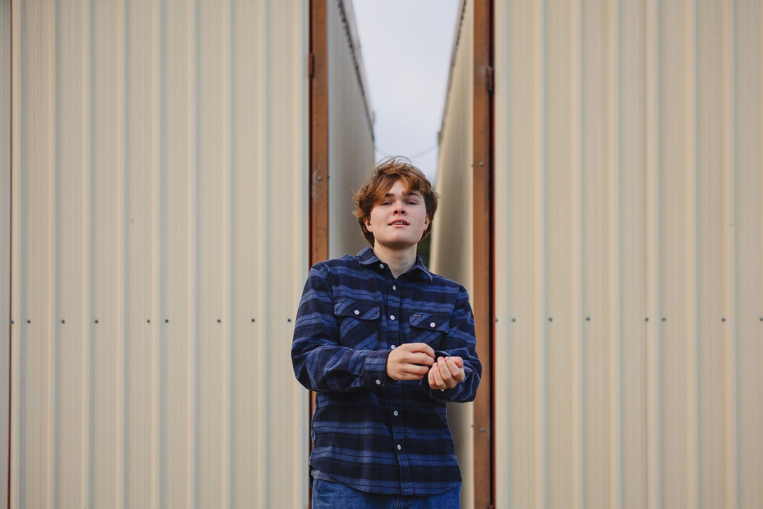Person in navy blue plaid shirt stands against a beige wall while holding a phone.