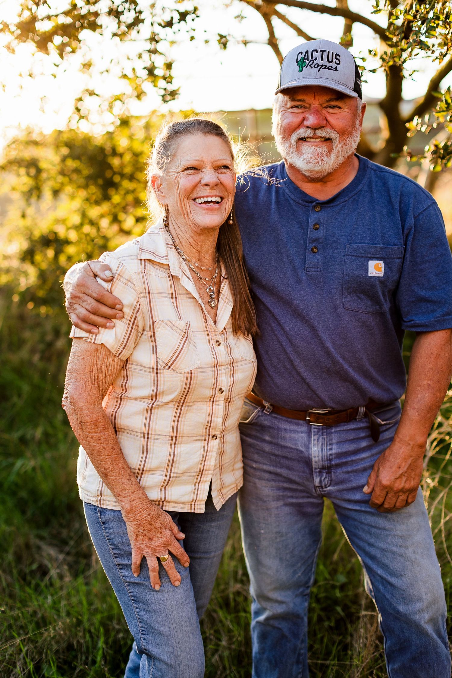 A couple stands together outdoors during golden hour light, with one wearing a plaid shirt and another in blue.