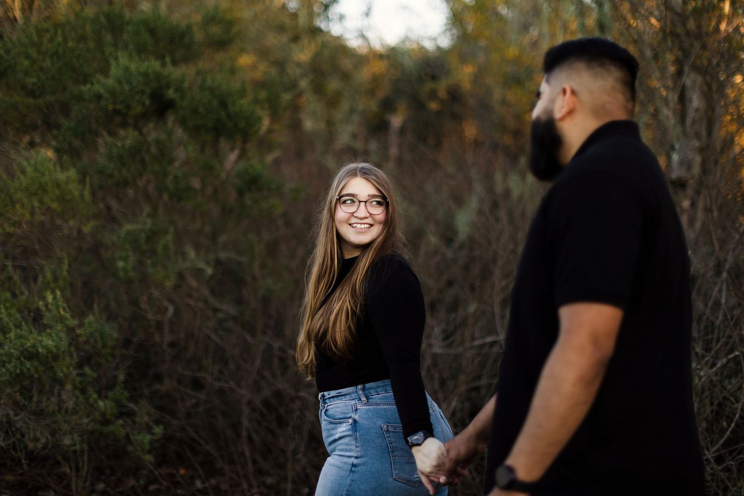 A couple walks together through an outdoor area with autumn trees in the background.