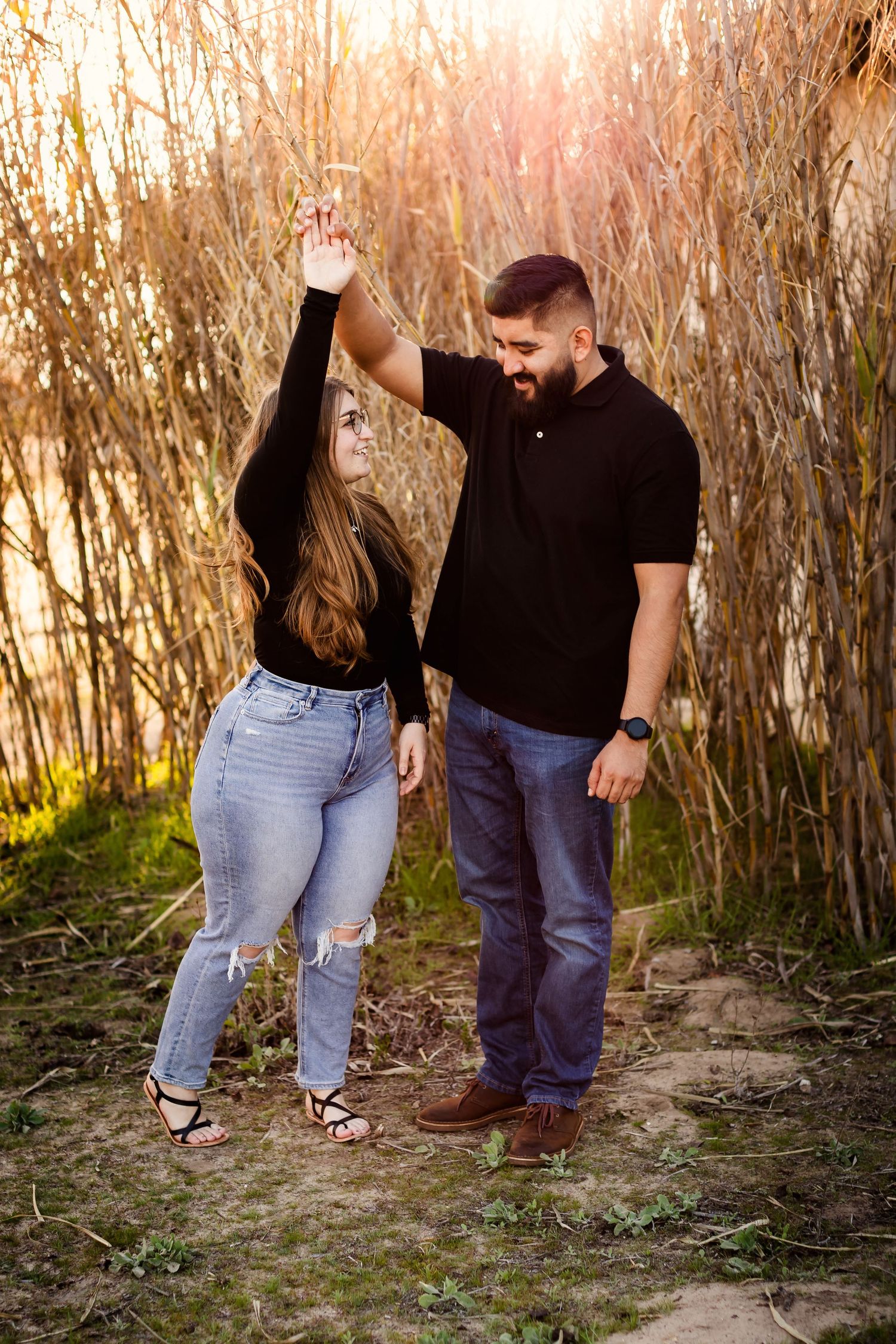 A couple enjoys a romantic moment together in front of tall dried reeds at sunset.