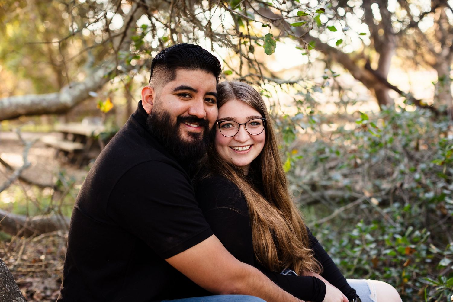 Couple snuggling and laughing together during an outdoor photo session in a wooded setting.