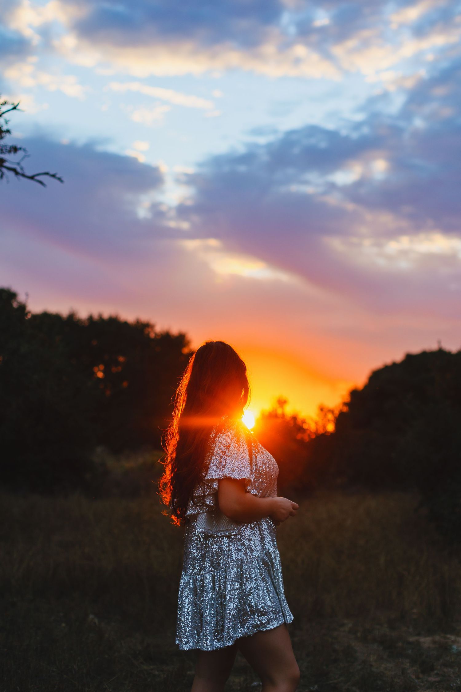 Silhouette of person in dress against dramatic orange and purple sunset sky.