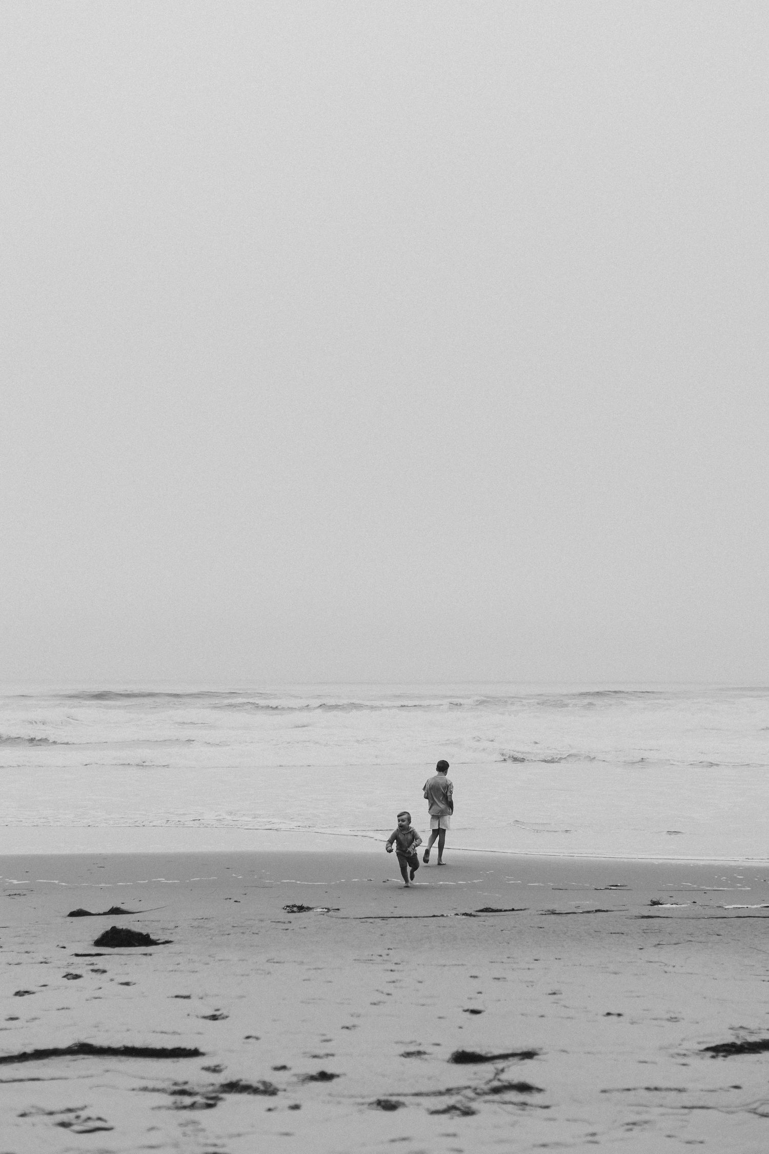 Black and white photo of two figures walking with dog on misty beach.