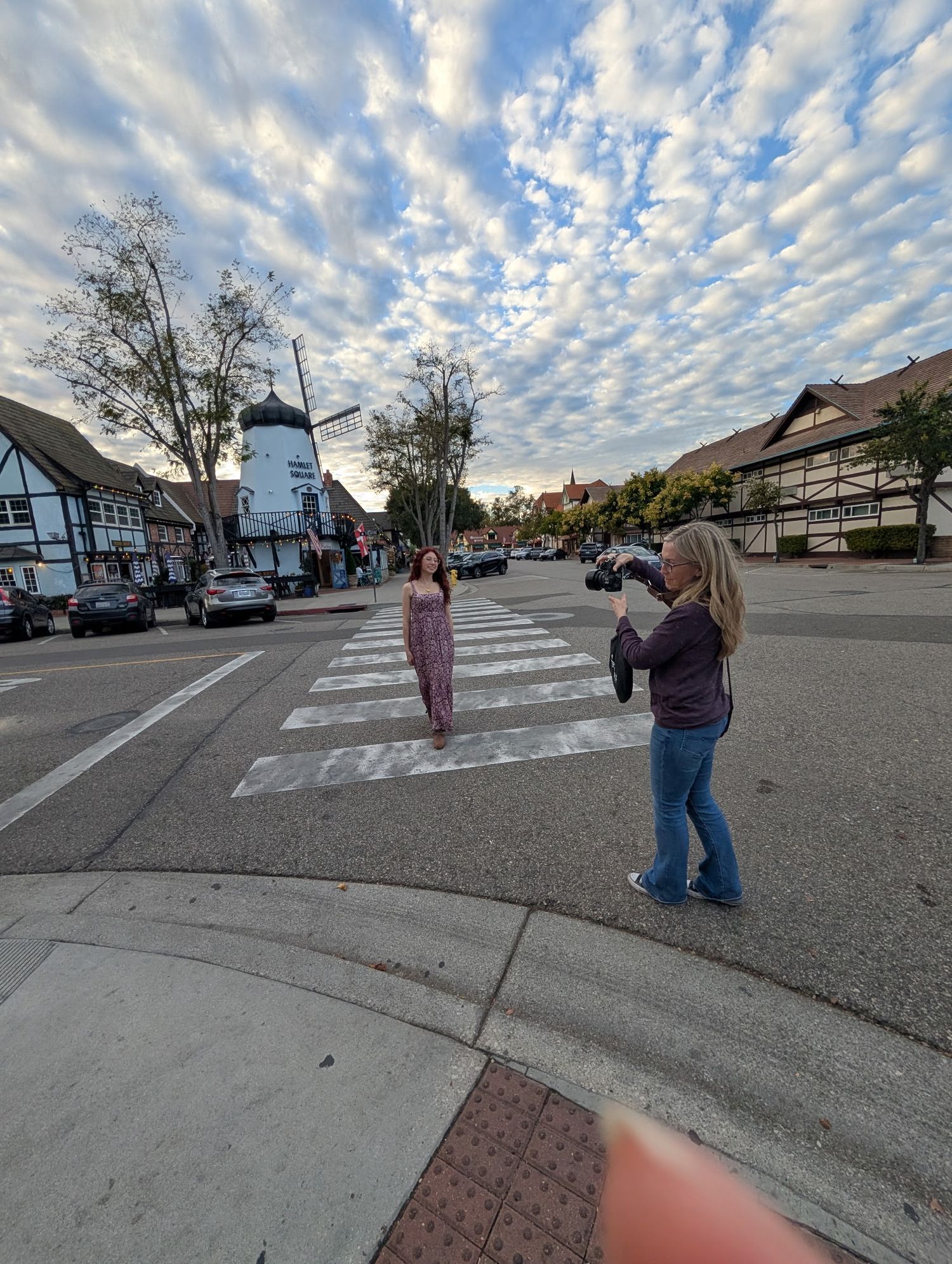 Photographer shooting model on crosswalk in Solvang with windmill and dramatic cloudy sky.