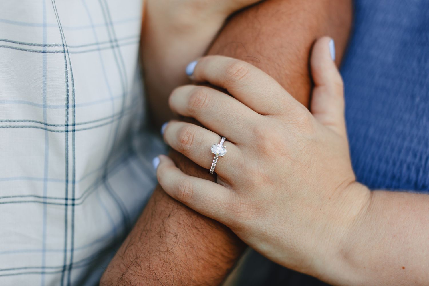 Close up of engagement ring as woman's hand rests on partner's arm.