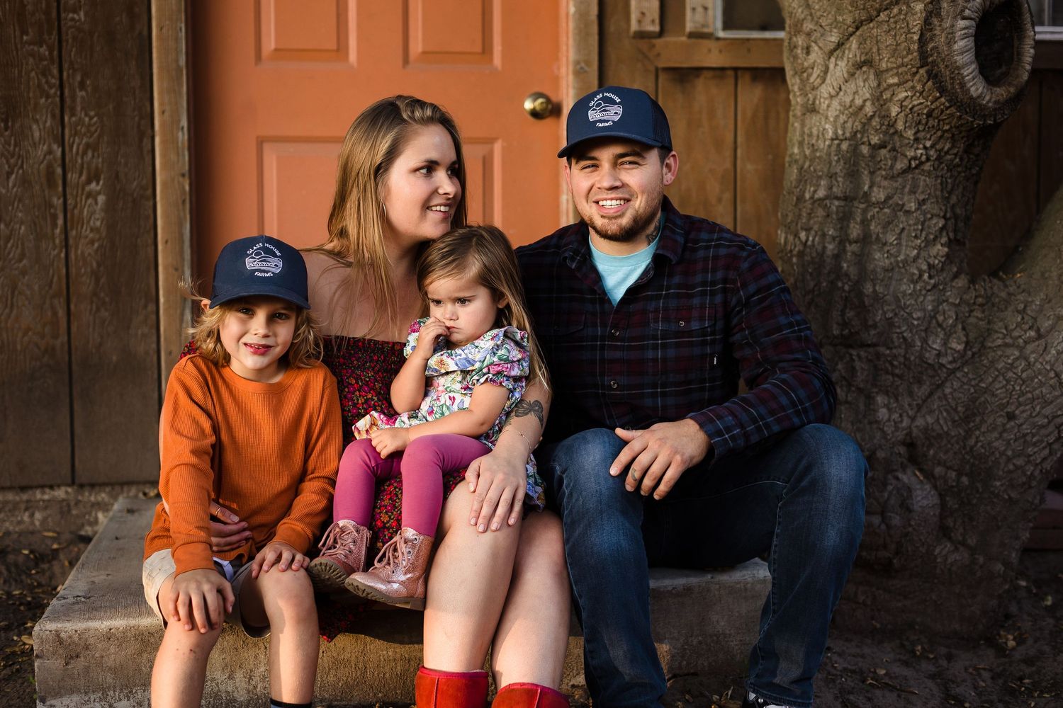 Family sits together on outdoor porch steps during autumn wearing casual clothing and baseball caps.