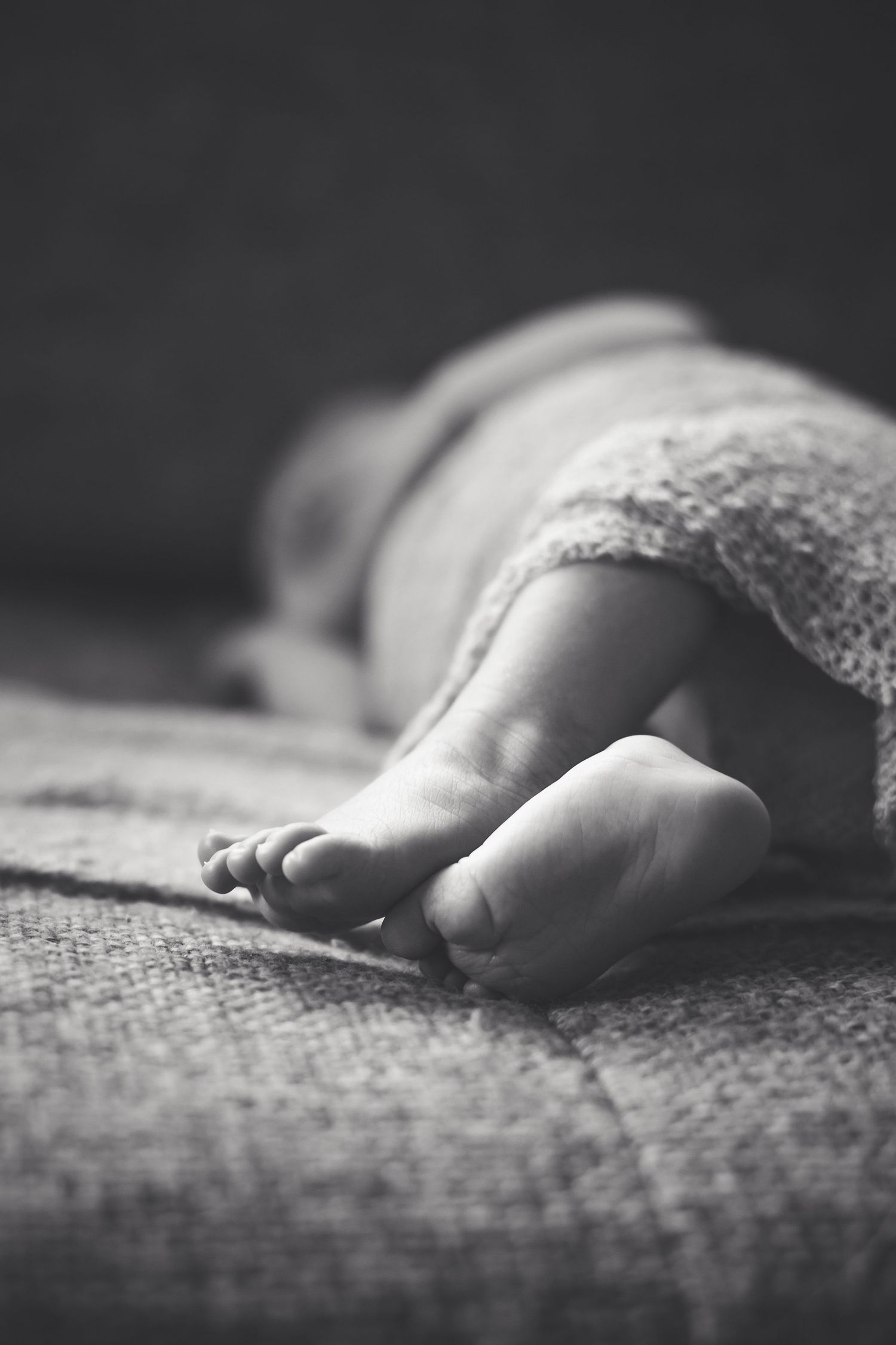 Close-up black and white photo of baby feet on textured blanket.