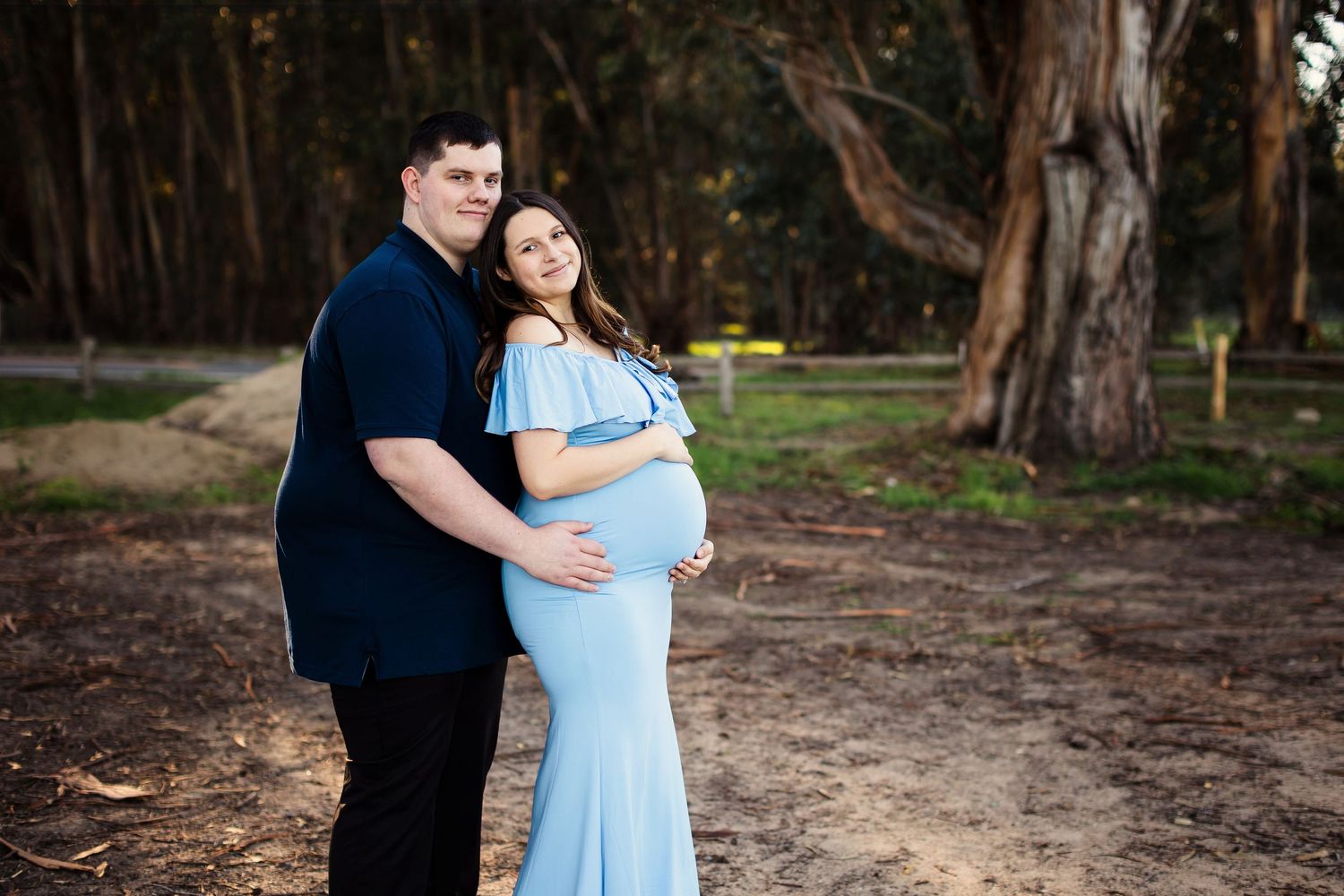 Couple shares romantic embrace in outdoor wooded setting wearing blue and navy coordinated outfits.