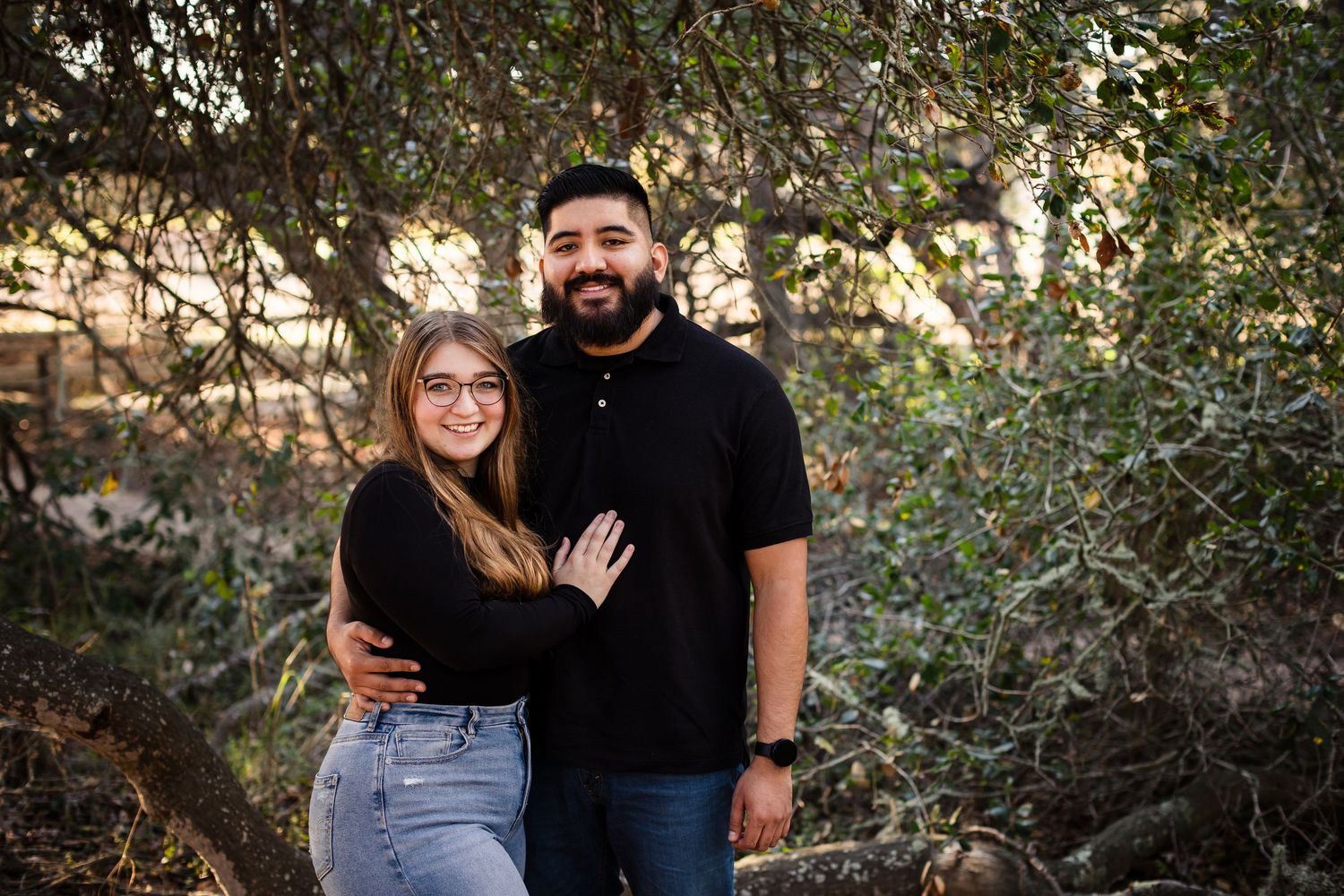 A loving couple embraces outdoors among greenery during a romantic photoshoot session at sunset.