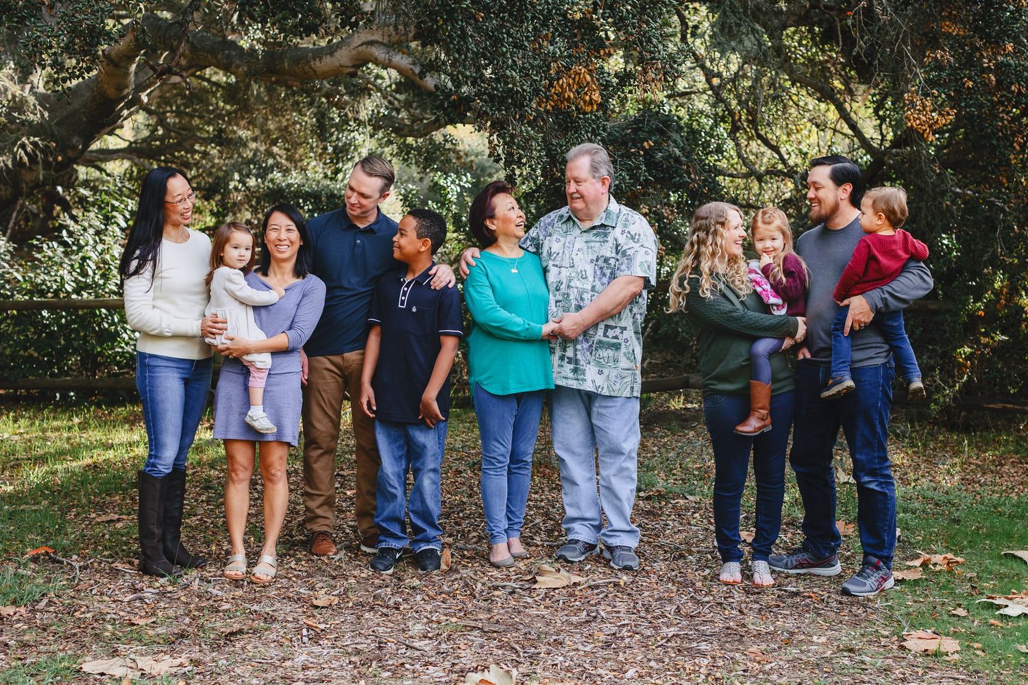 A group of people standing together outdoors under trees on a sunny day in casual attire.