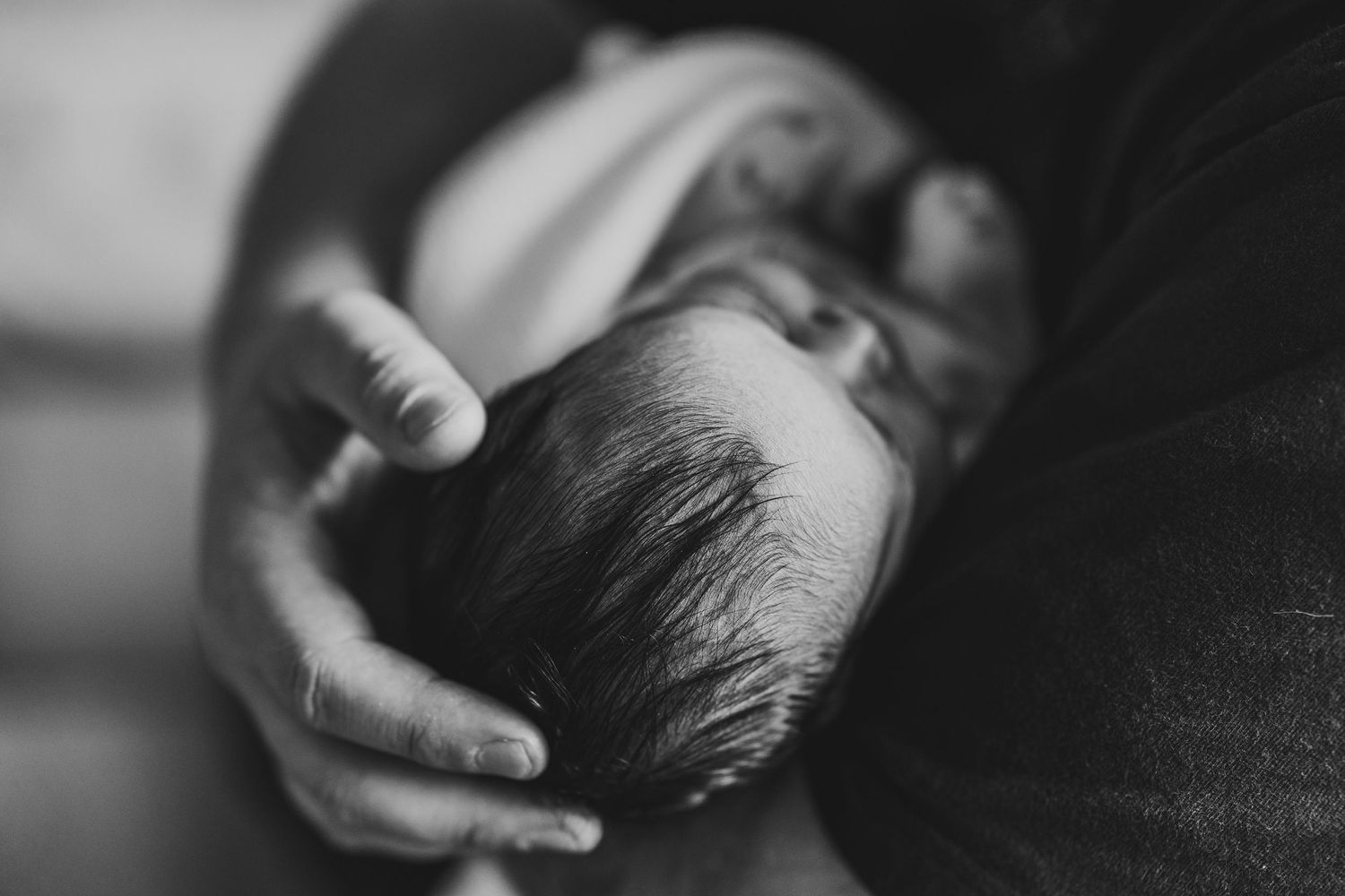Black and white photo of a newborn baby cradled gently in an adults hands, showcasing delicate features and tiny fingers.
