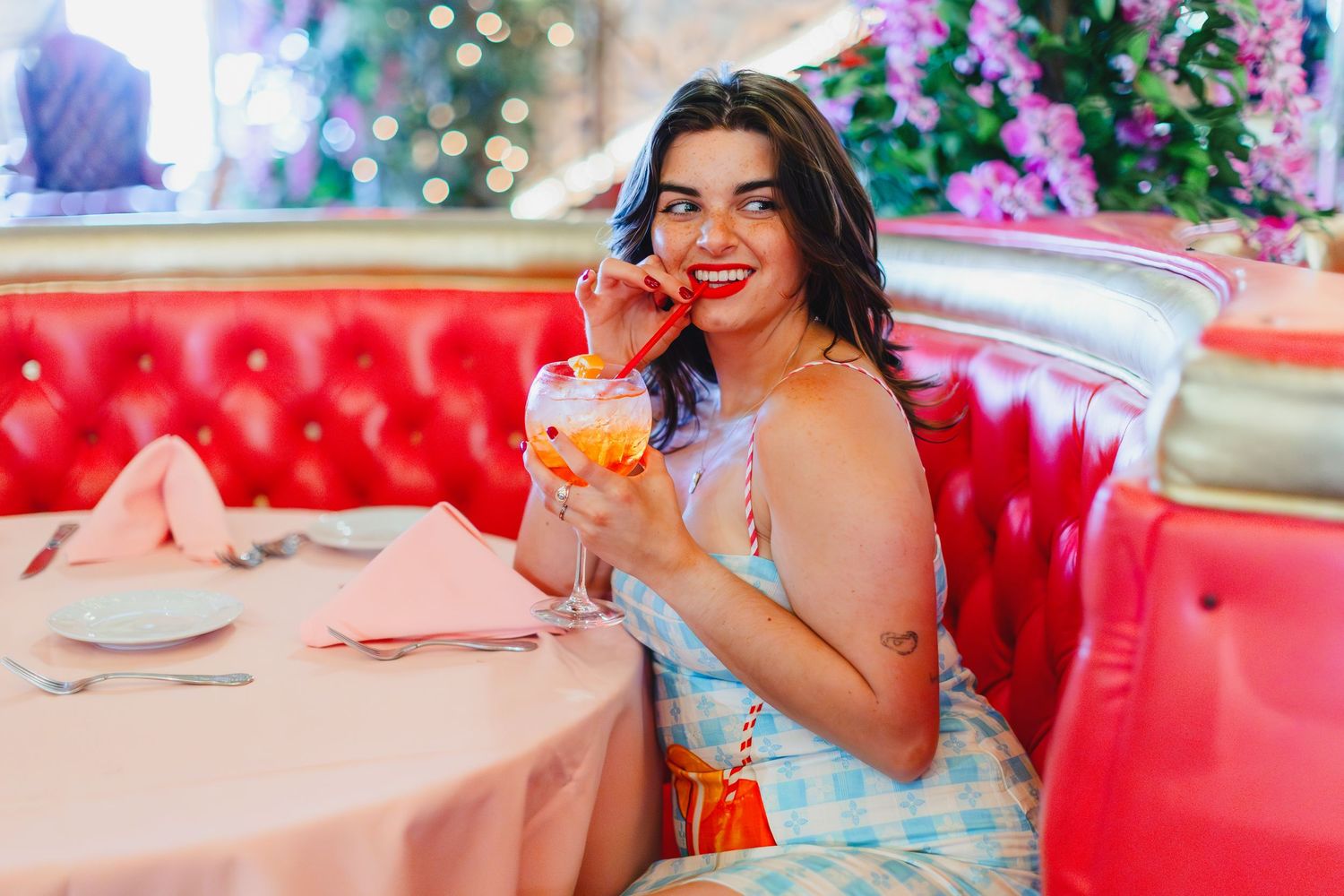 Someone enjoys a colorful cocktail while seated in a bright red booth with soft lighting and holiday decorations.