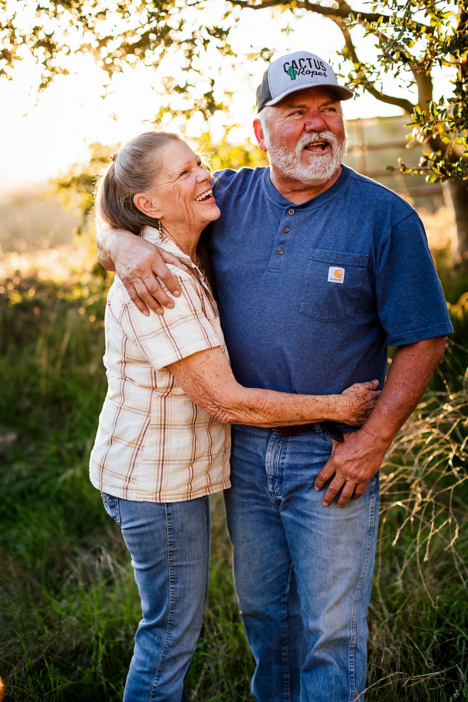 Happy couple laughing together in a field at sunset during casual outdoor photoshoot.