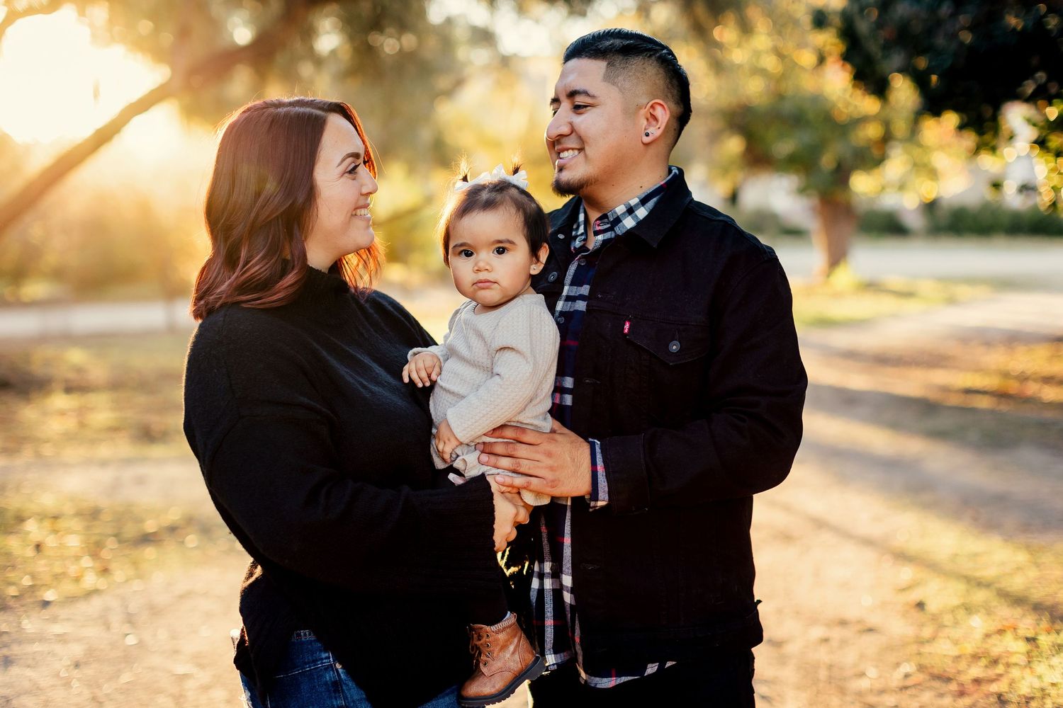 A loving family of three shares tender moments together in a sunny outdoor setting during golden hour.