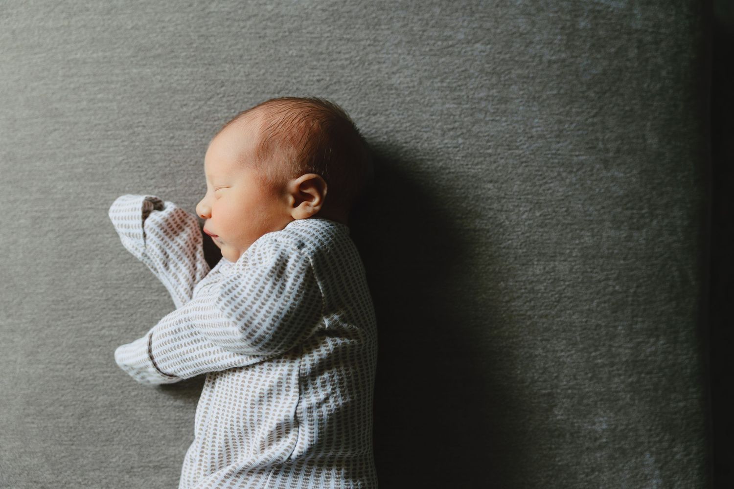 Newborn baby sleeping peacefully on a gray surface wearing a striped onesie.