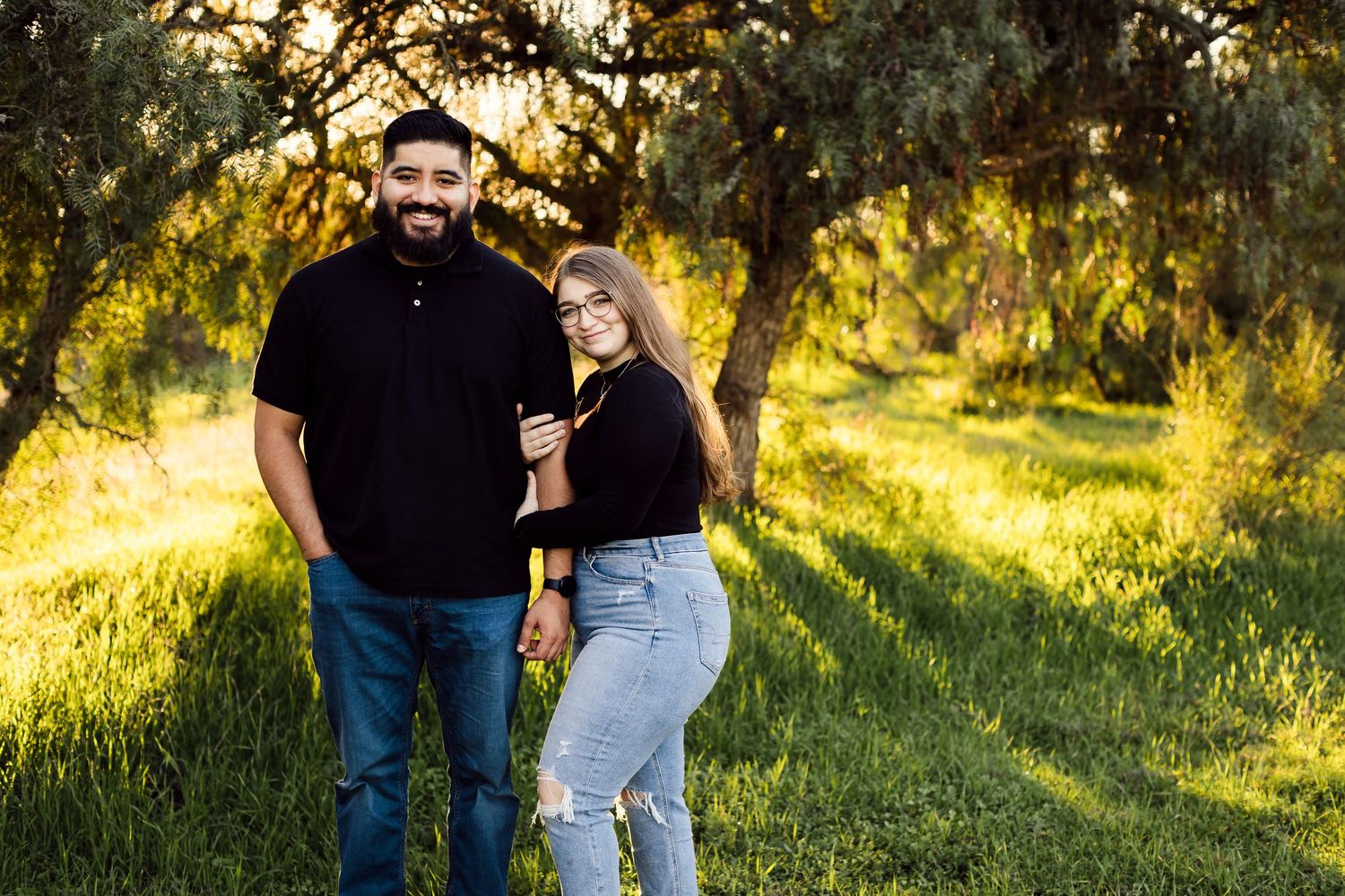 A romantic couple enjoys a tender moment outdoors in a sunlit field at golden hour.