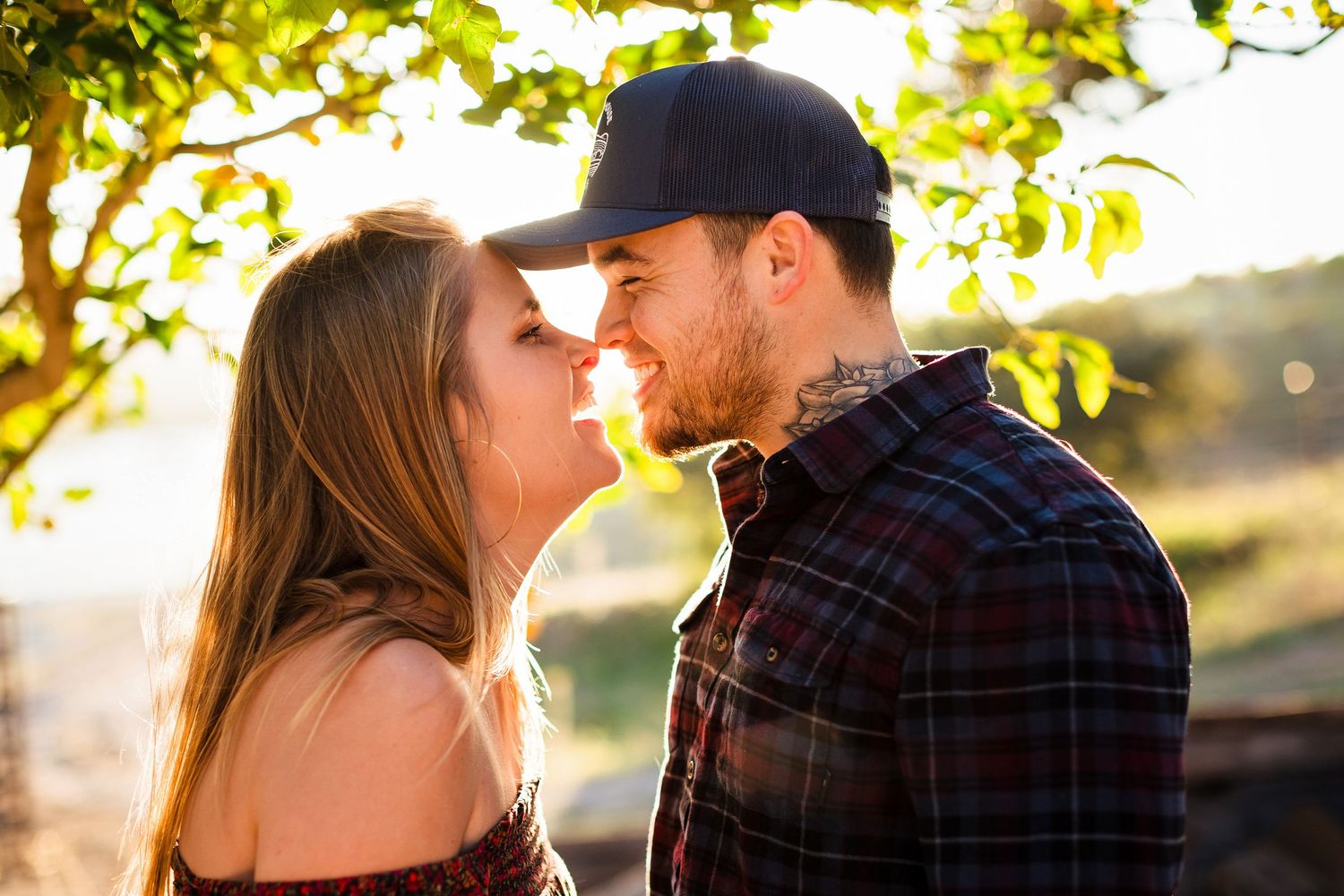 A romantic couple shares an intimate moment during sunset in a park setting, backlit by warm golden sunlight.