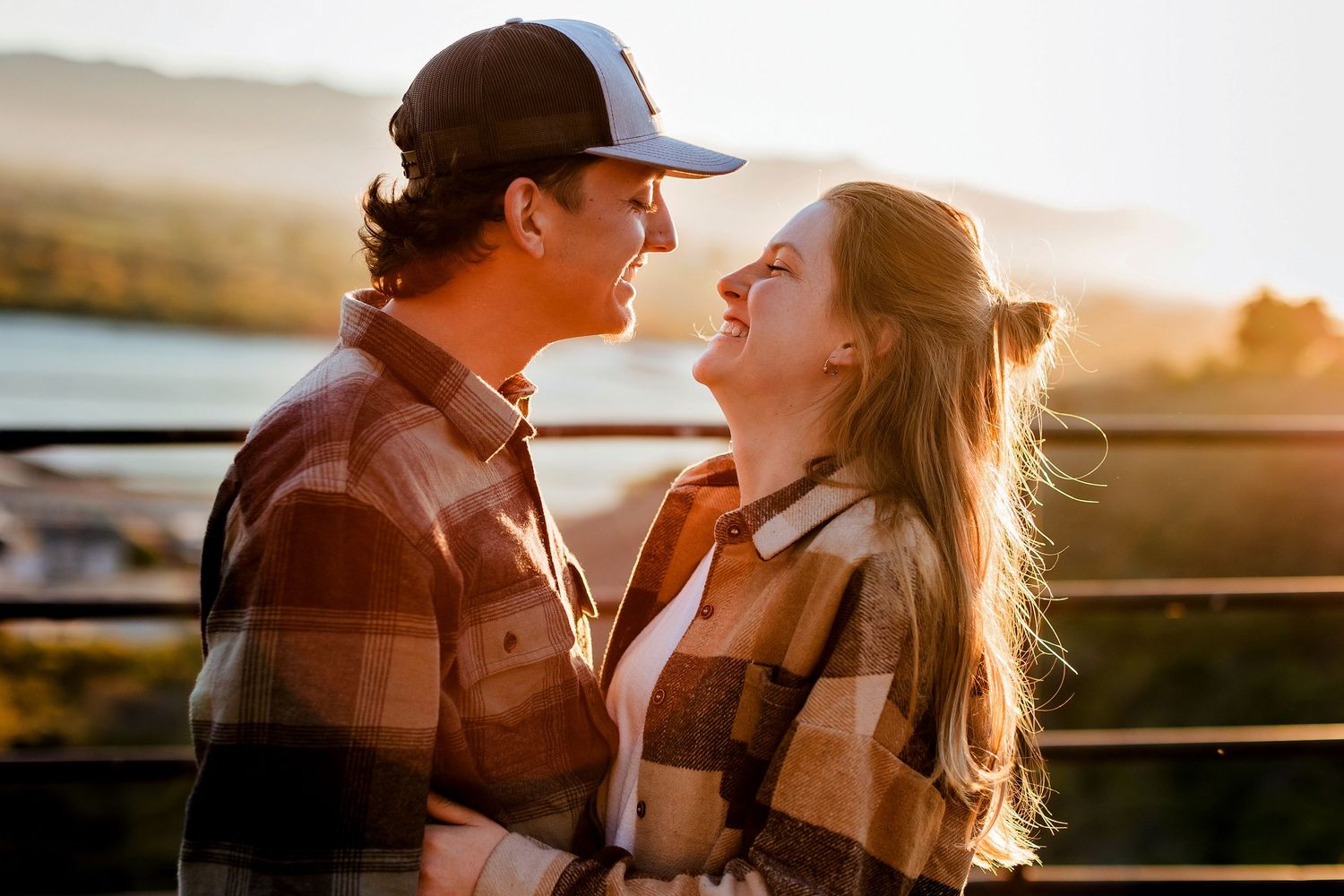 Silhouetted couple sharing intimate moments during golden hour sunset by a rustic fence.