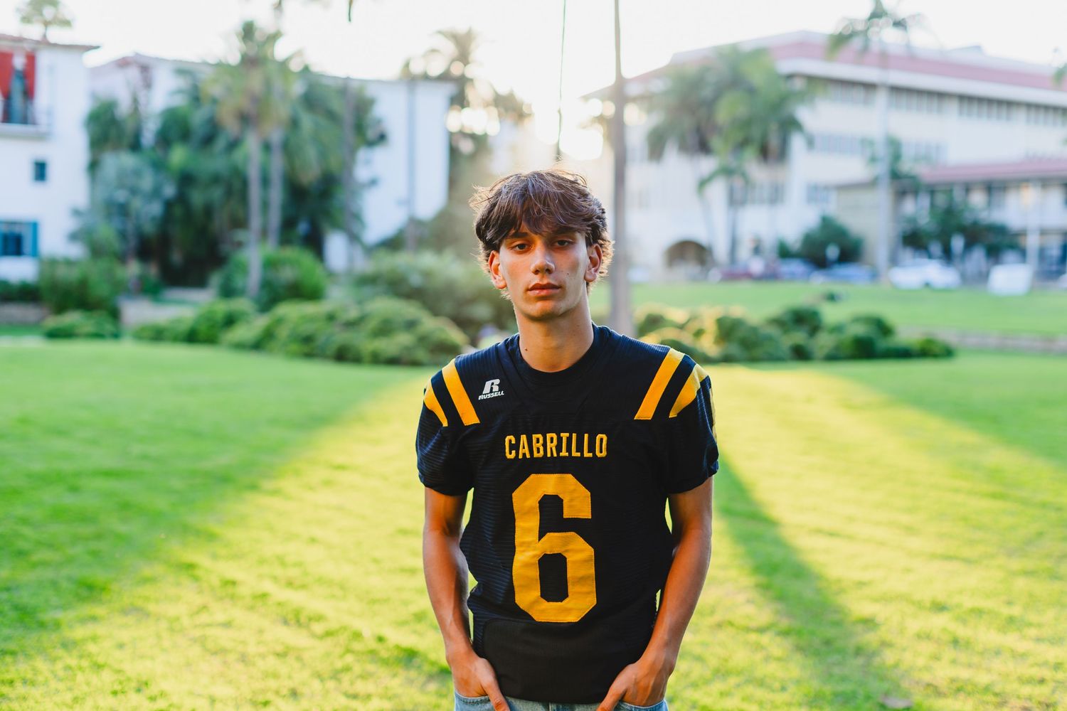 Football player wearing black and yellow jersey with number 6 stands on grassy field.