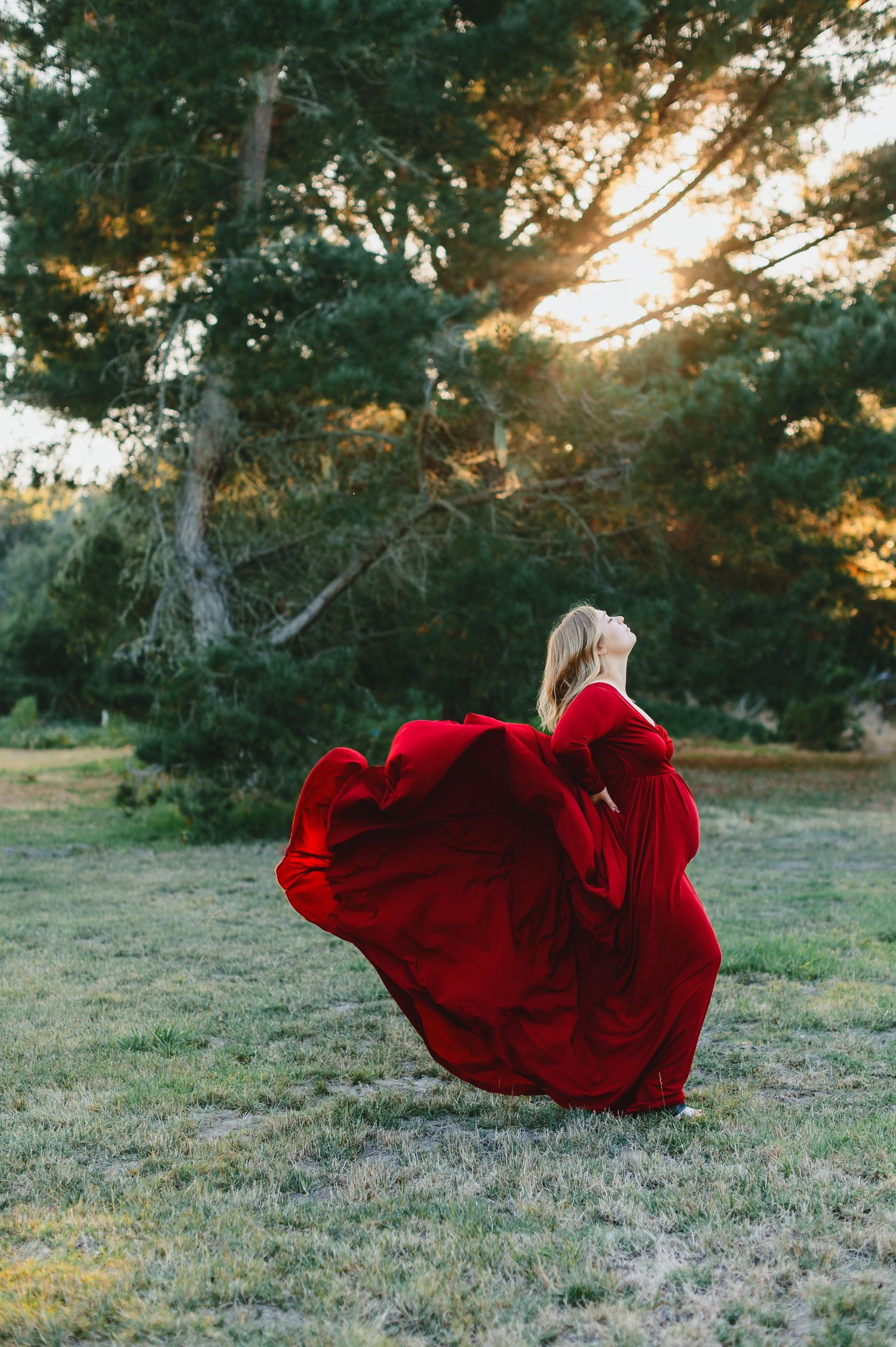 Person in flowing red dress twirls dramatically at sunset in a grassy field.