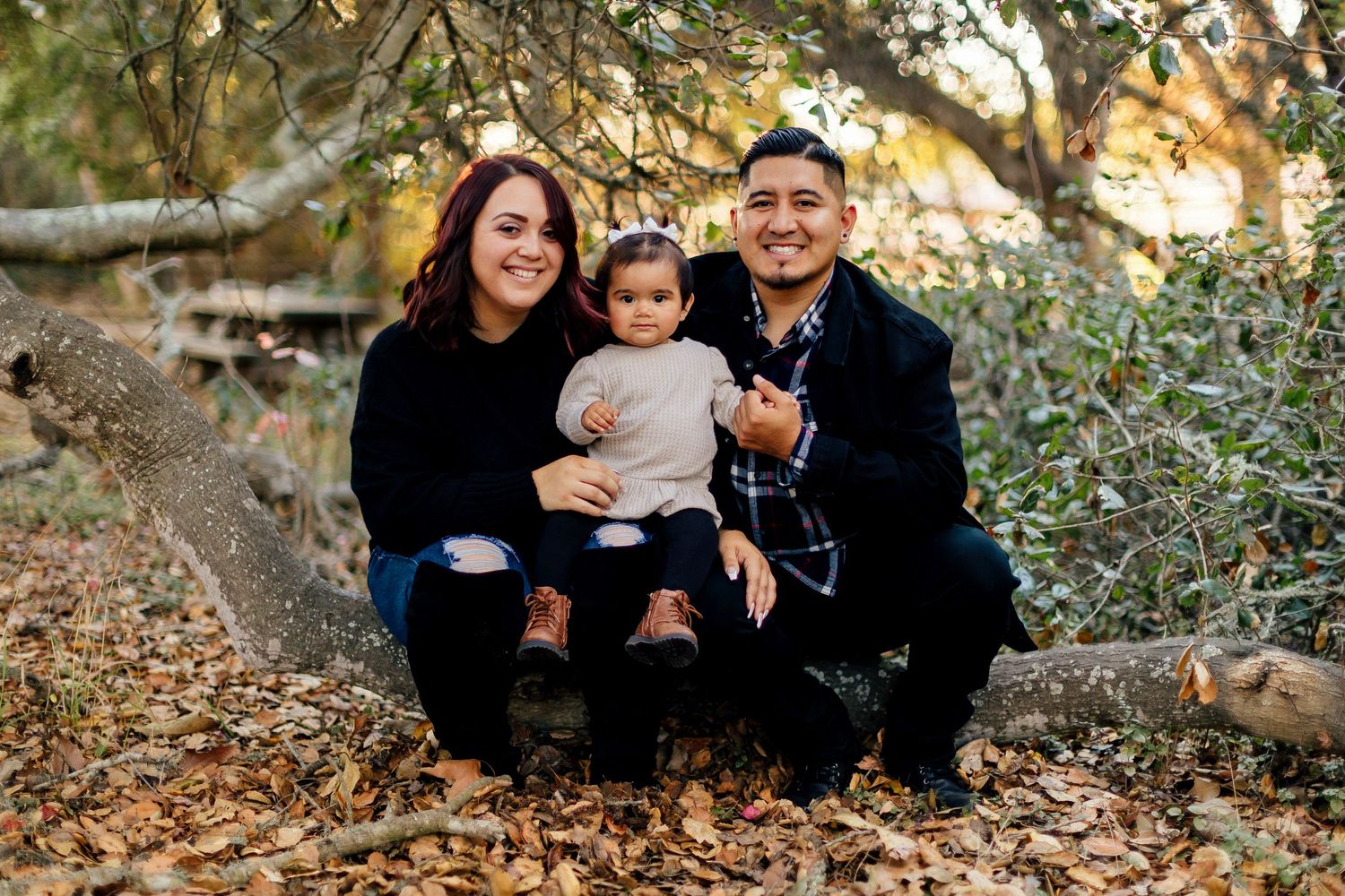 A relaxed outdoor family photo session captured in warm autumn sunlight among fallen leaves.